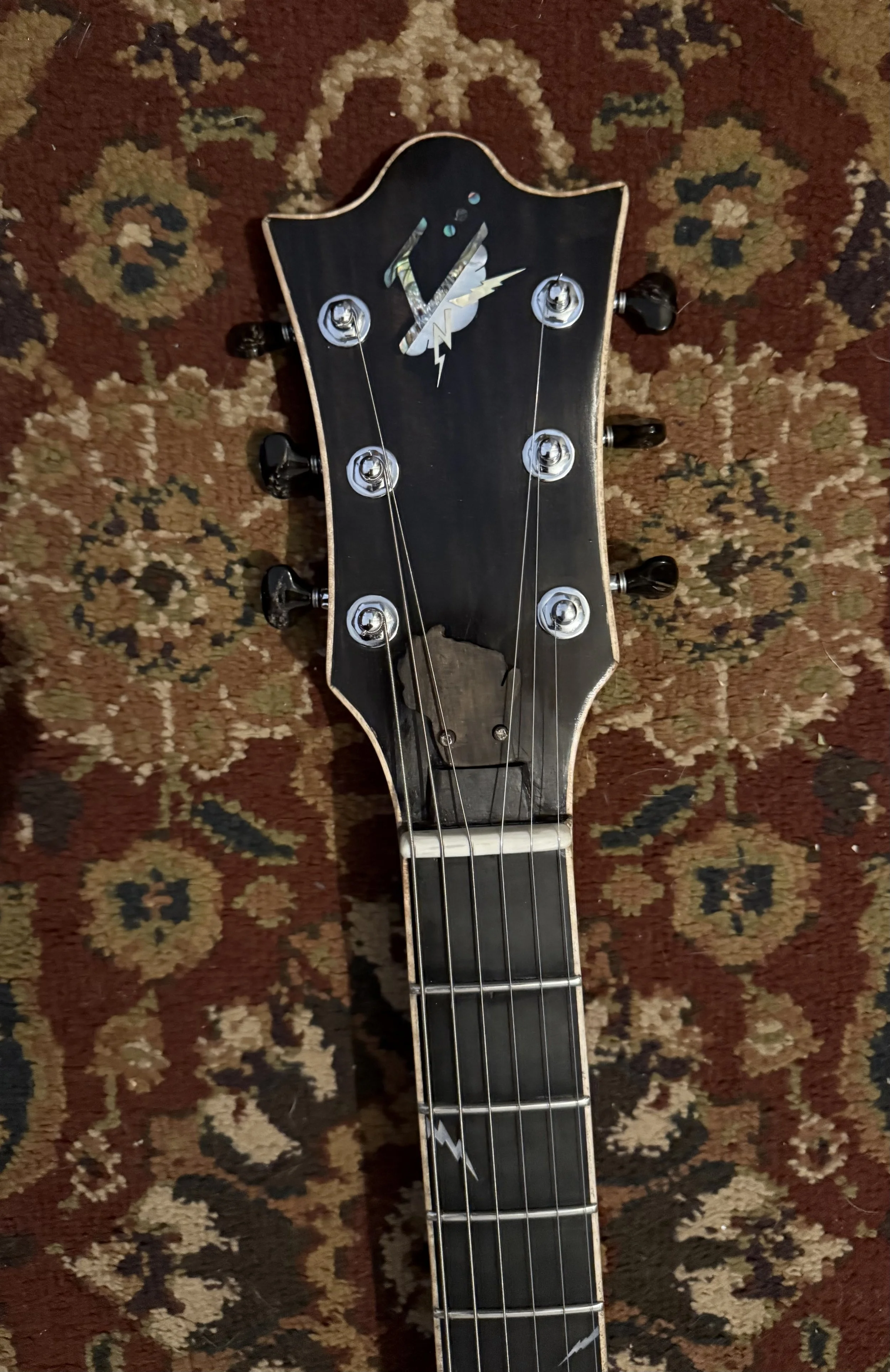 Headstock of a guitar with a lightning bolt design and a lightning bolt inlay, resting on a patterned rug.