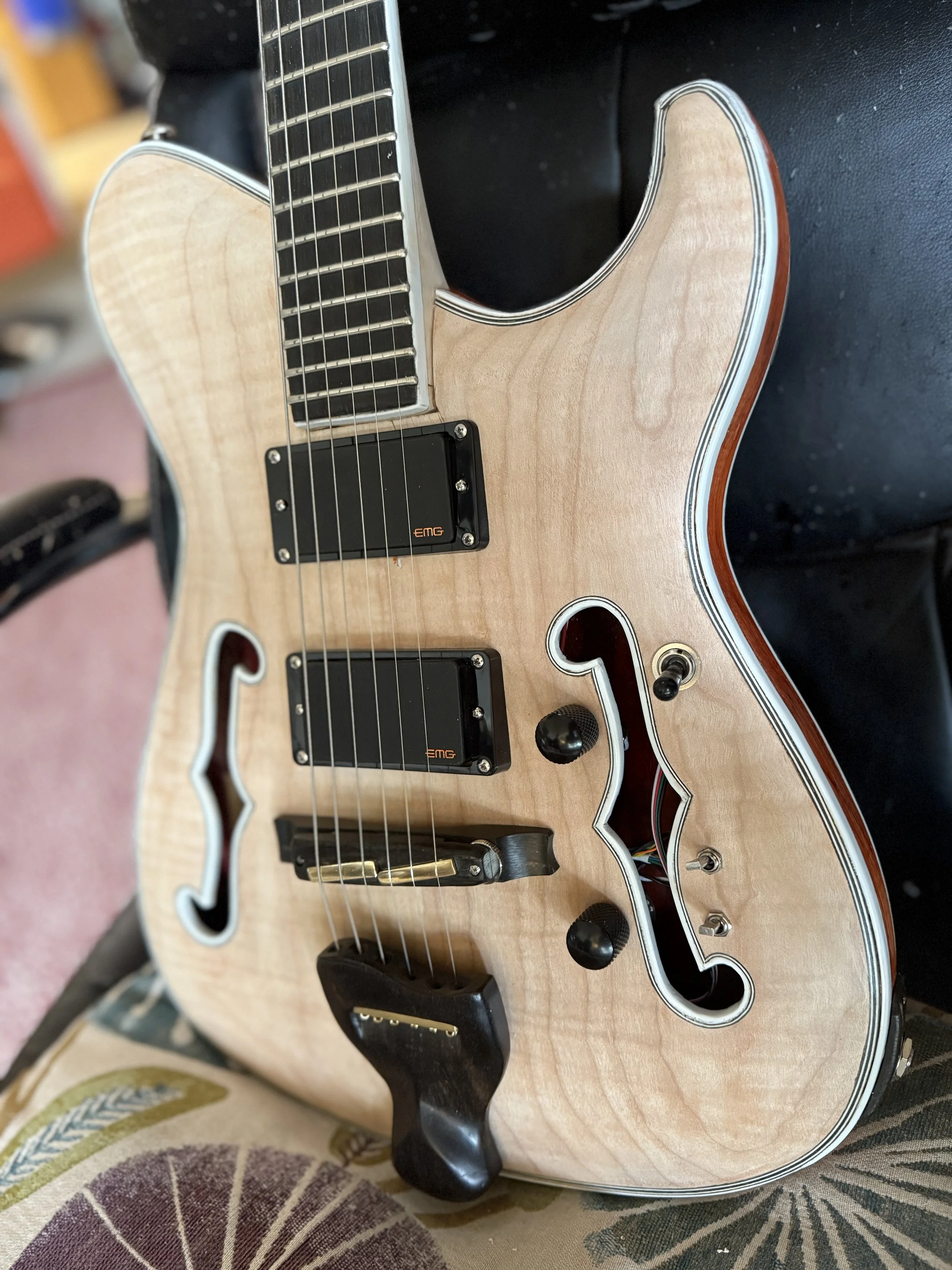An electric guitar with a natural wood finish, black hardware, and black pickups, resting on a black surface.