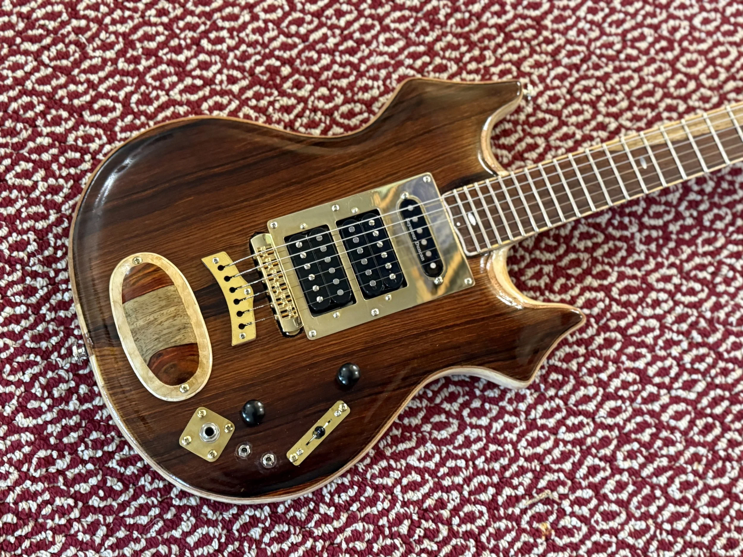 Close-up of a brown electric guitar with gold hardware lying on a red and white patterned carpet.
