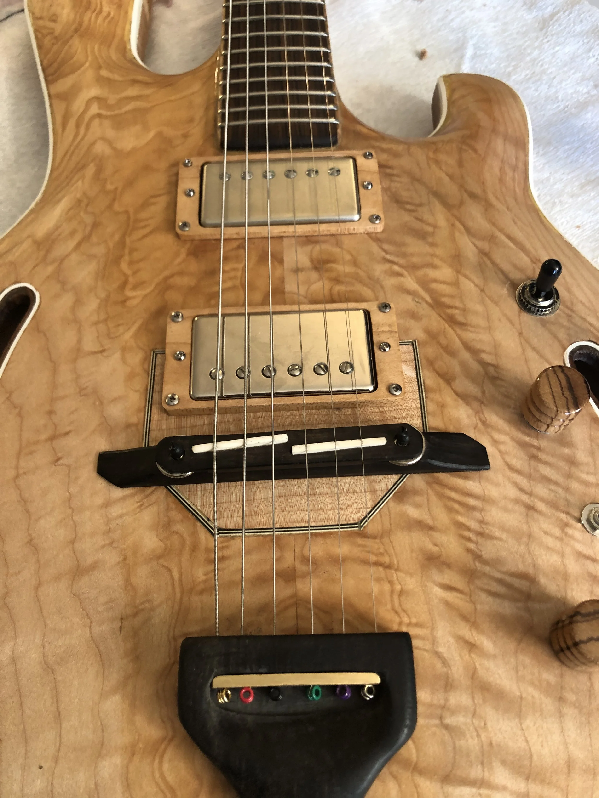 Close-up of a wooden electric guitar with six strings, pickups, a black bridge, and control knobs on a wooden surface.