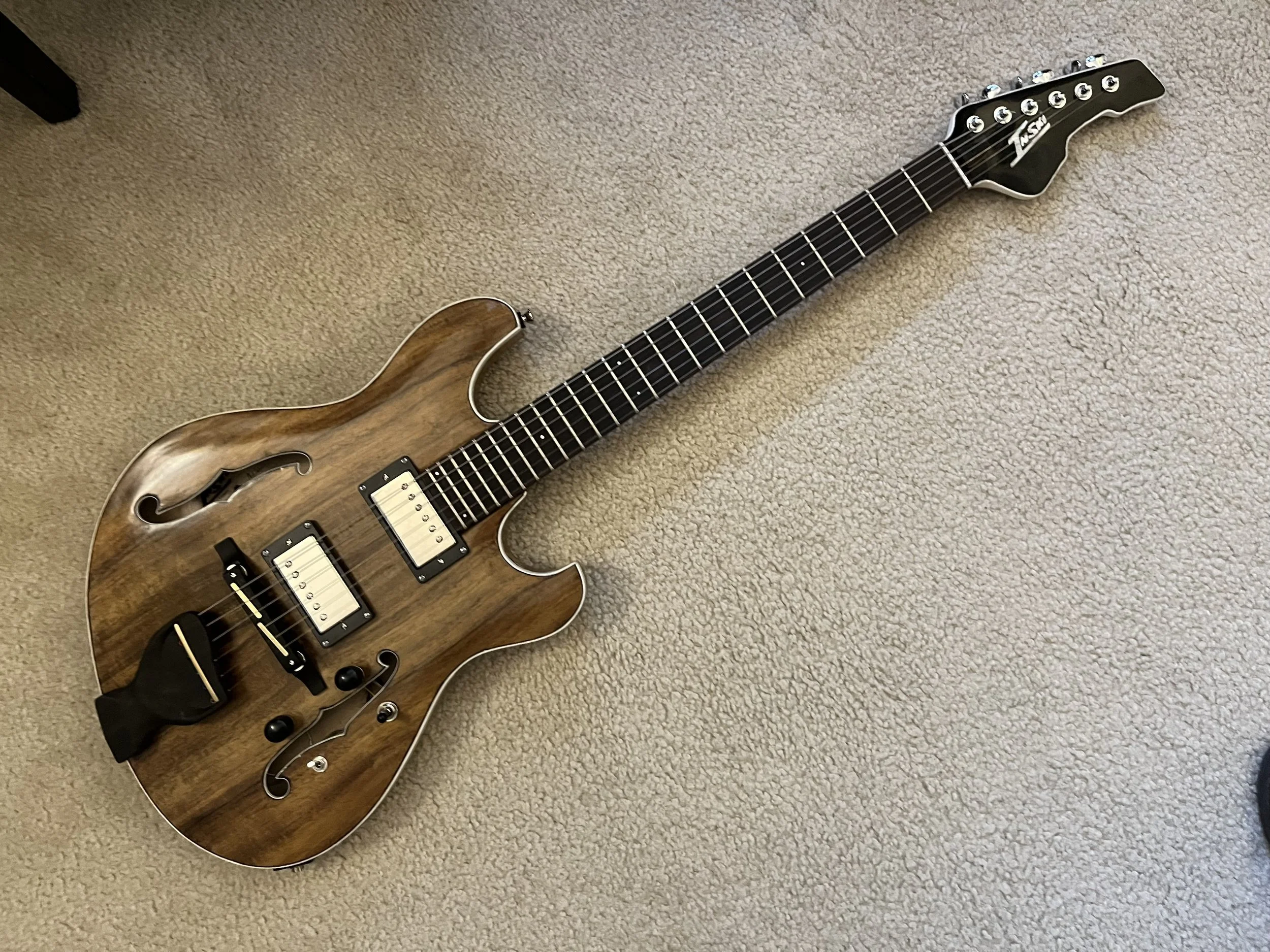 An electric guitar with a wooden finish lying on a beige carpeted floor.