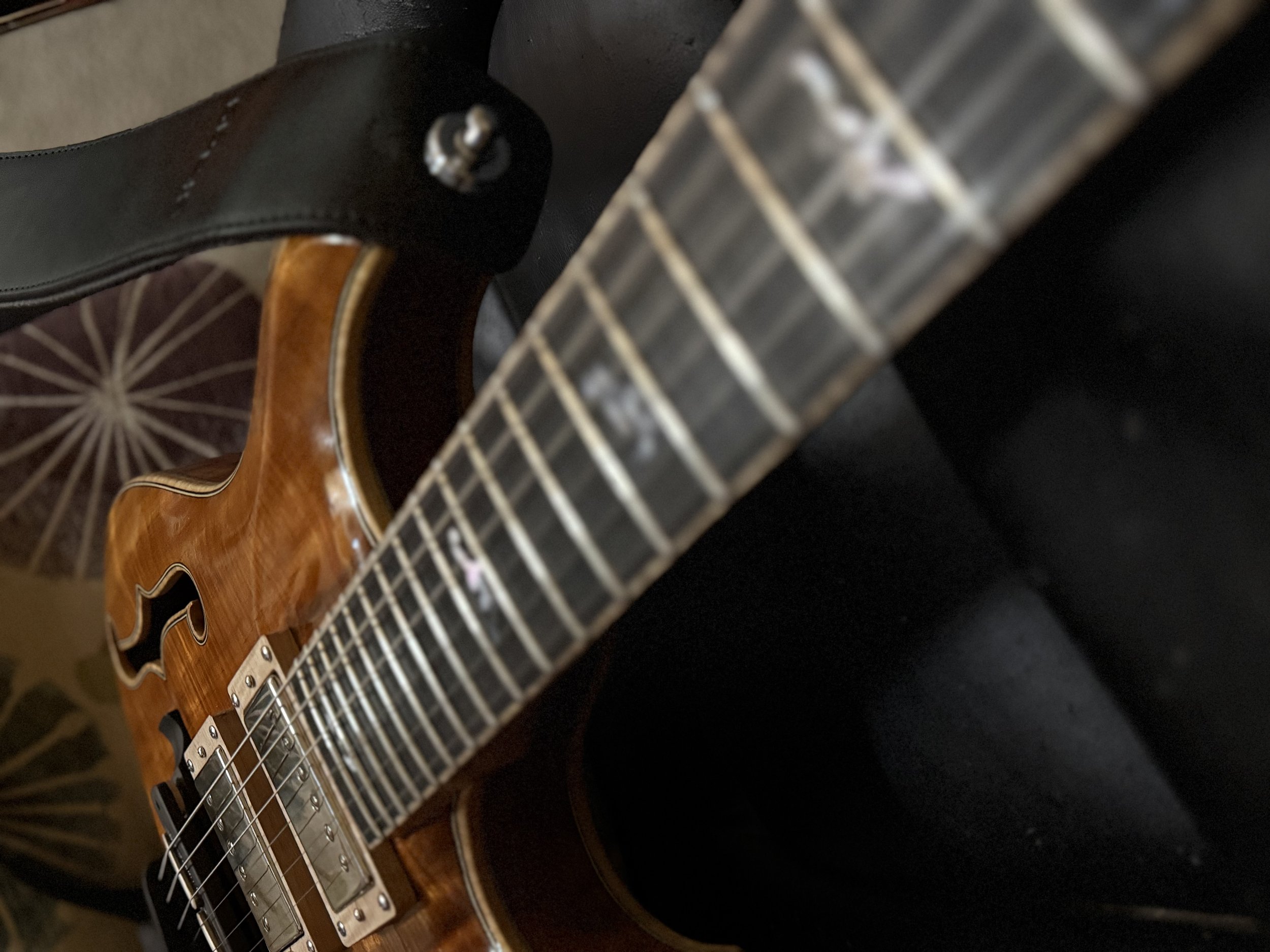 Close-up of an electric guitar body with a wooden finish, metal pickups, and strings, resting against a black guitar case on a patterned rug.