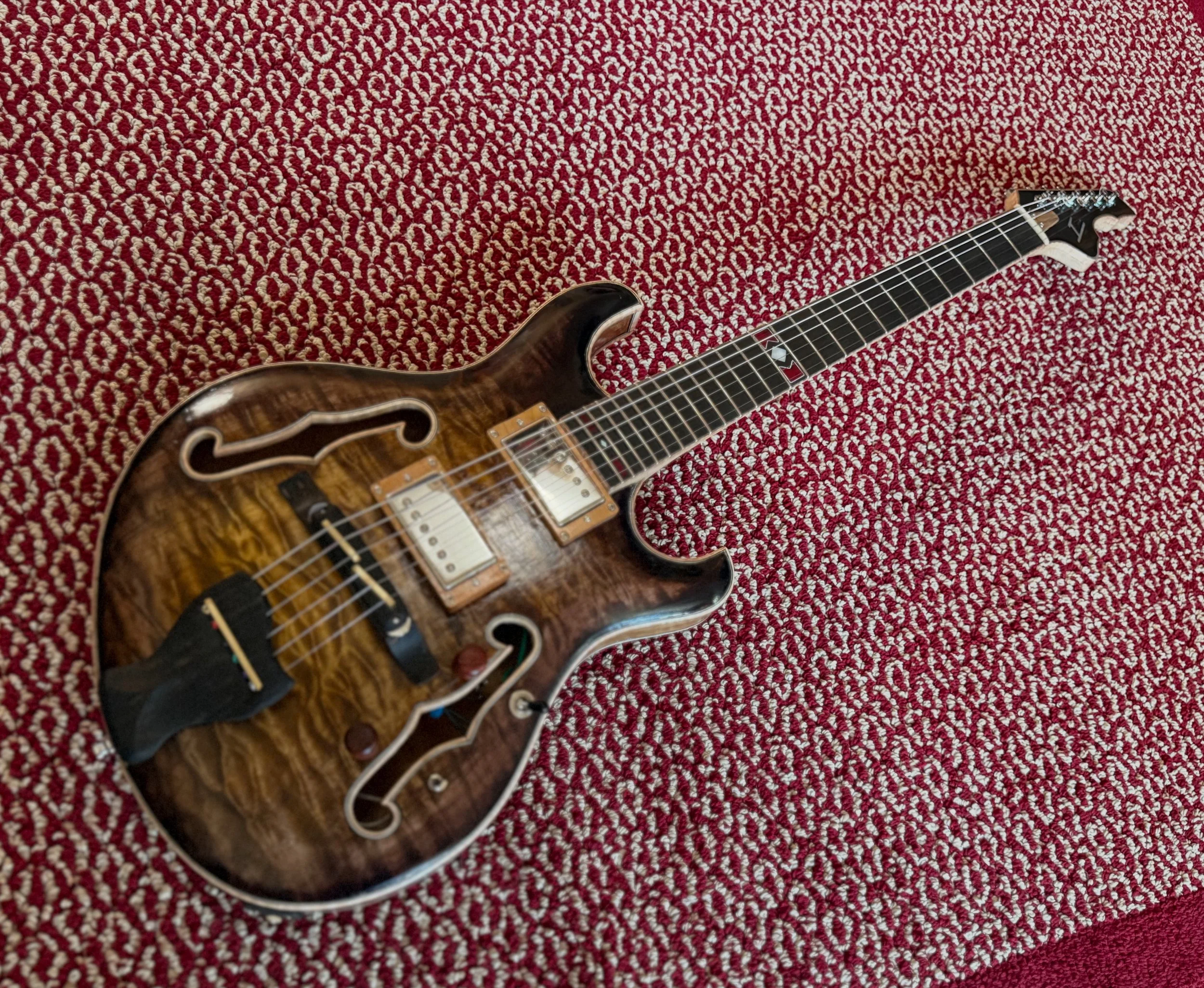 An electric guitar with a wood grain finish on a patterned red and white carpet.
