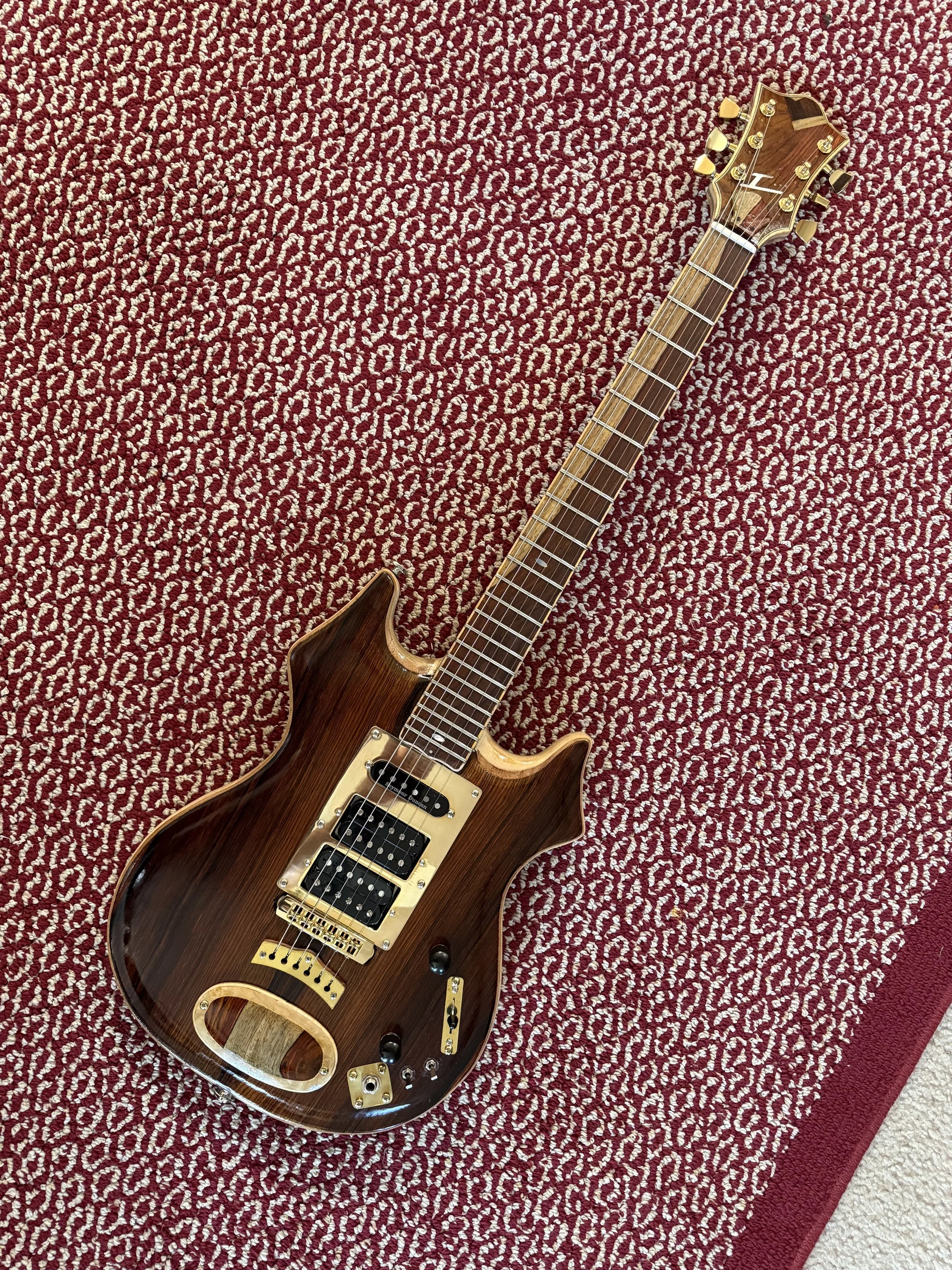 A brown electric guitar with gold hardware lying on a red and white patterned rug.