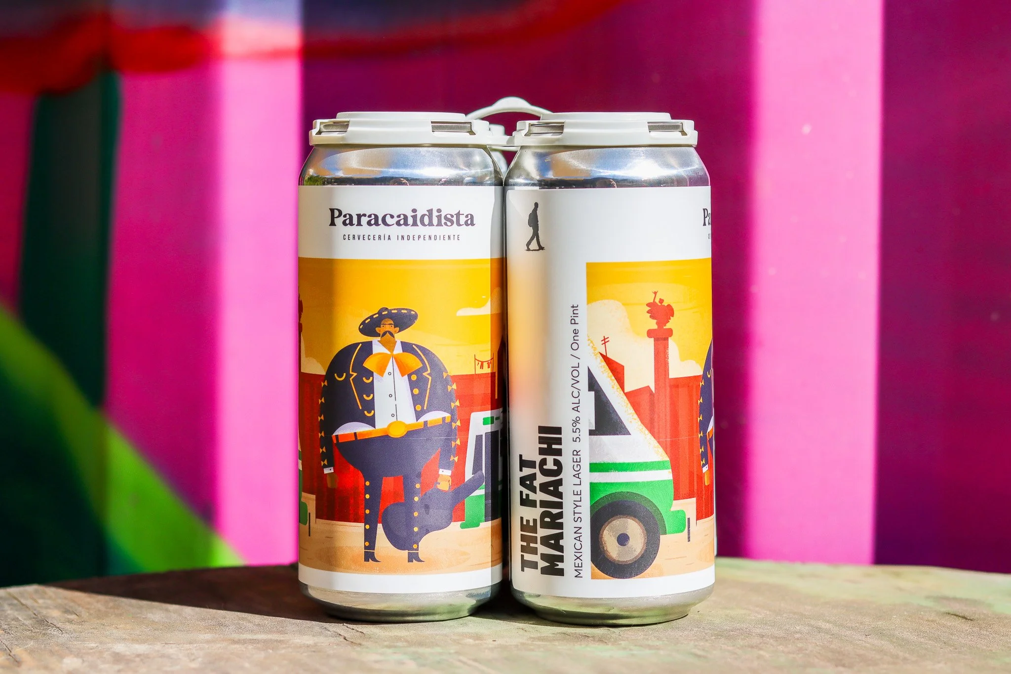 Four cans of Mexican style lager called "The Fat Mariachi" with colorful label art featuring a mariachi musician with a mustache, sombrero, and suit, standing against vibrant pink, green, and red background.