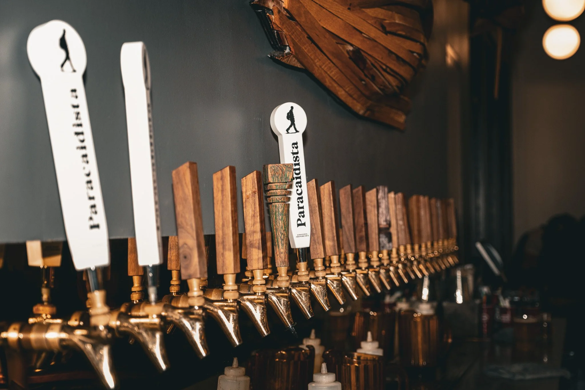Beer taps with wooden handles labeled 'Patrón Caribbean,' 'Paracaïsta,' and others in a bar or restaurant setting.