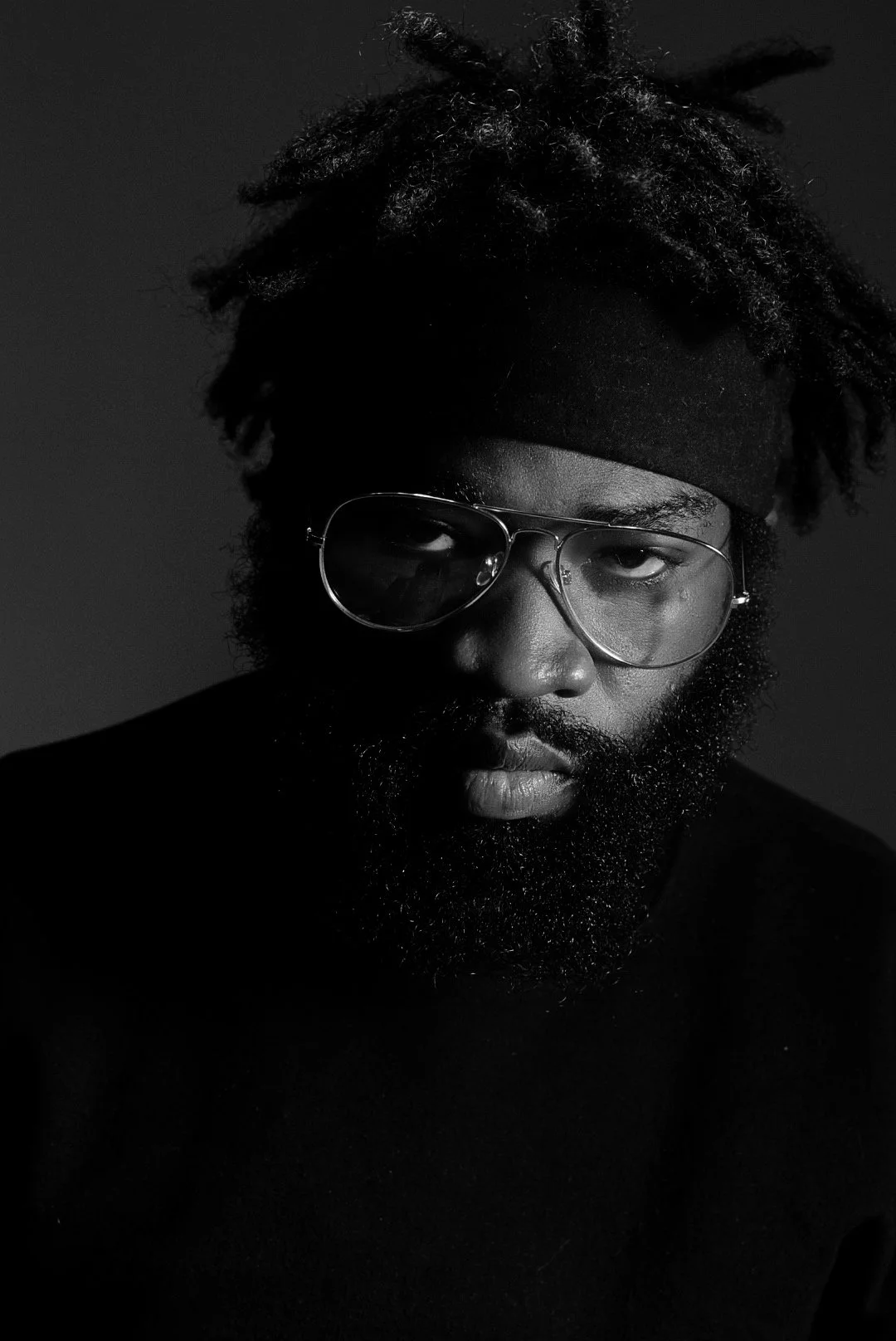 Black and white portrait of a man with a beard, wearing sunglasses and a headband, looking directly at the camera.