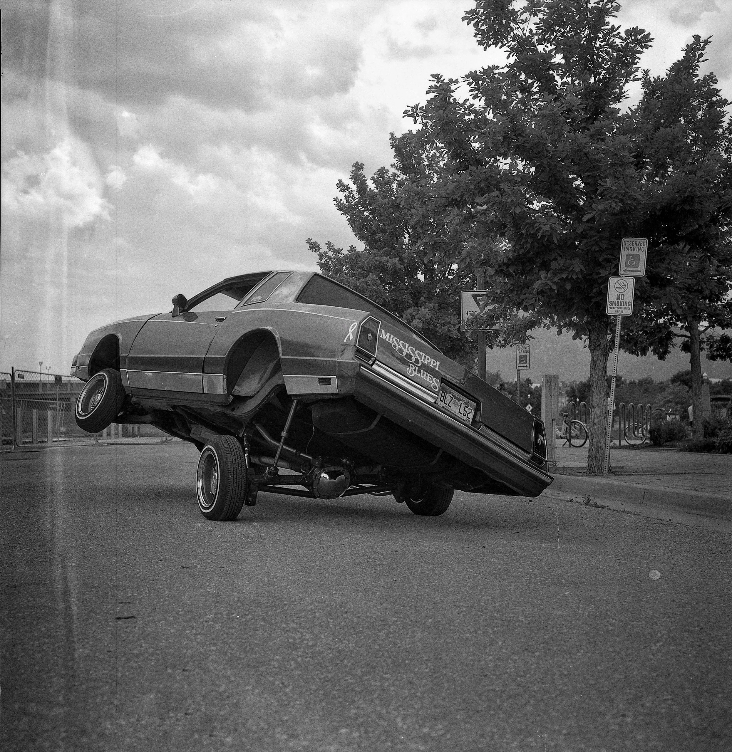 A car with a Mississippi Blues decal on its side is balancing on its front wheels on a street, with the rear wheels lifted off the ground.