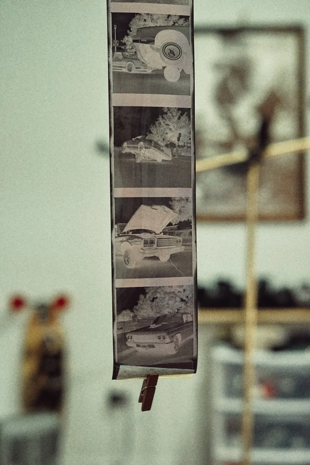 A strip of four black-and-white photographs showing different cars, hanging vertically in a room with blurred background.