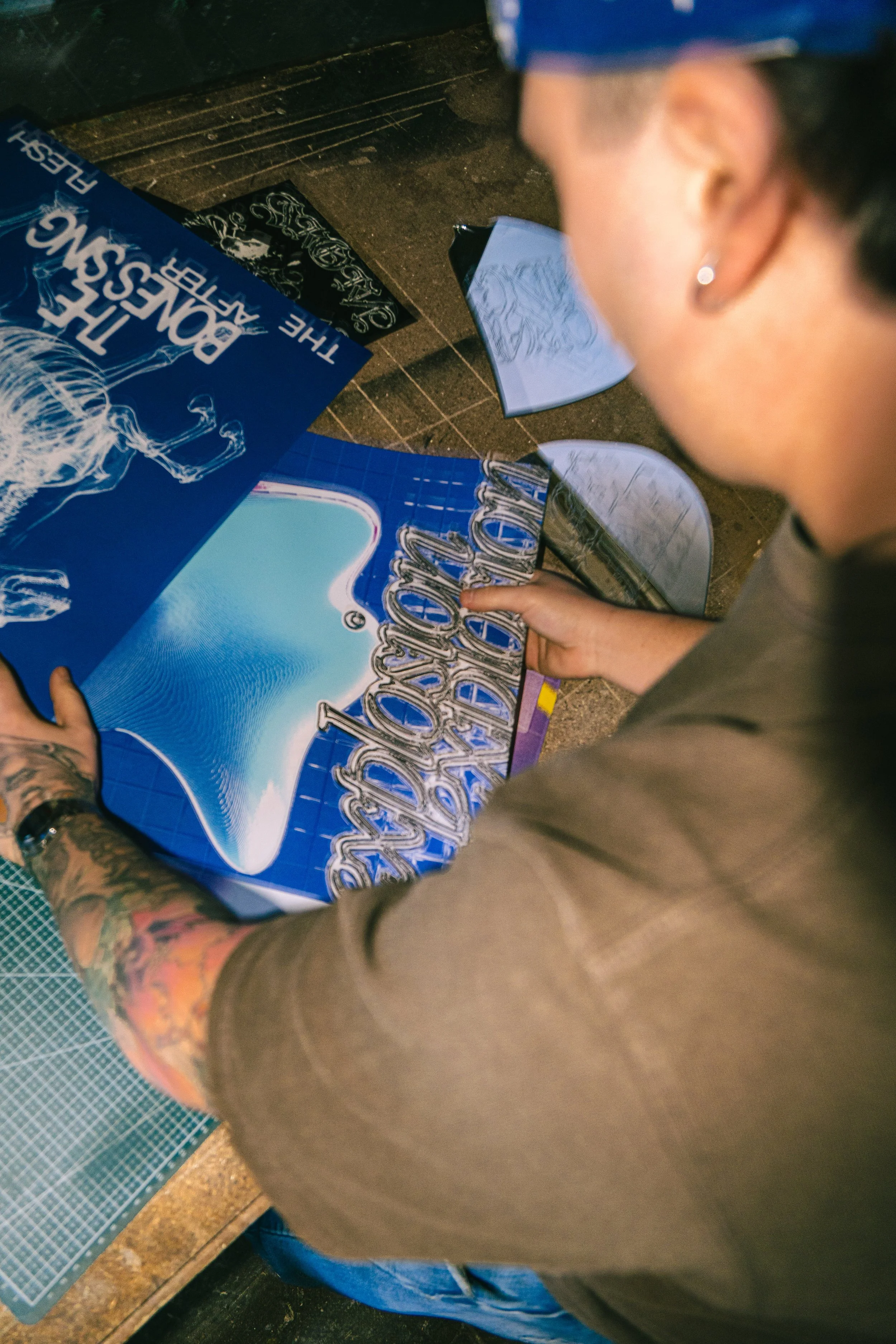 Une personne regarde une plaque de décoration avec l'inscription "The Bondage Art" et un squelette dessiné, en train de finir ou de manipuler la plaque.