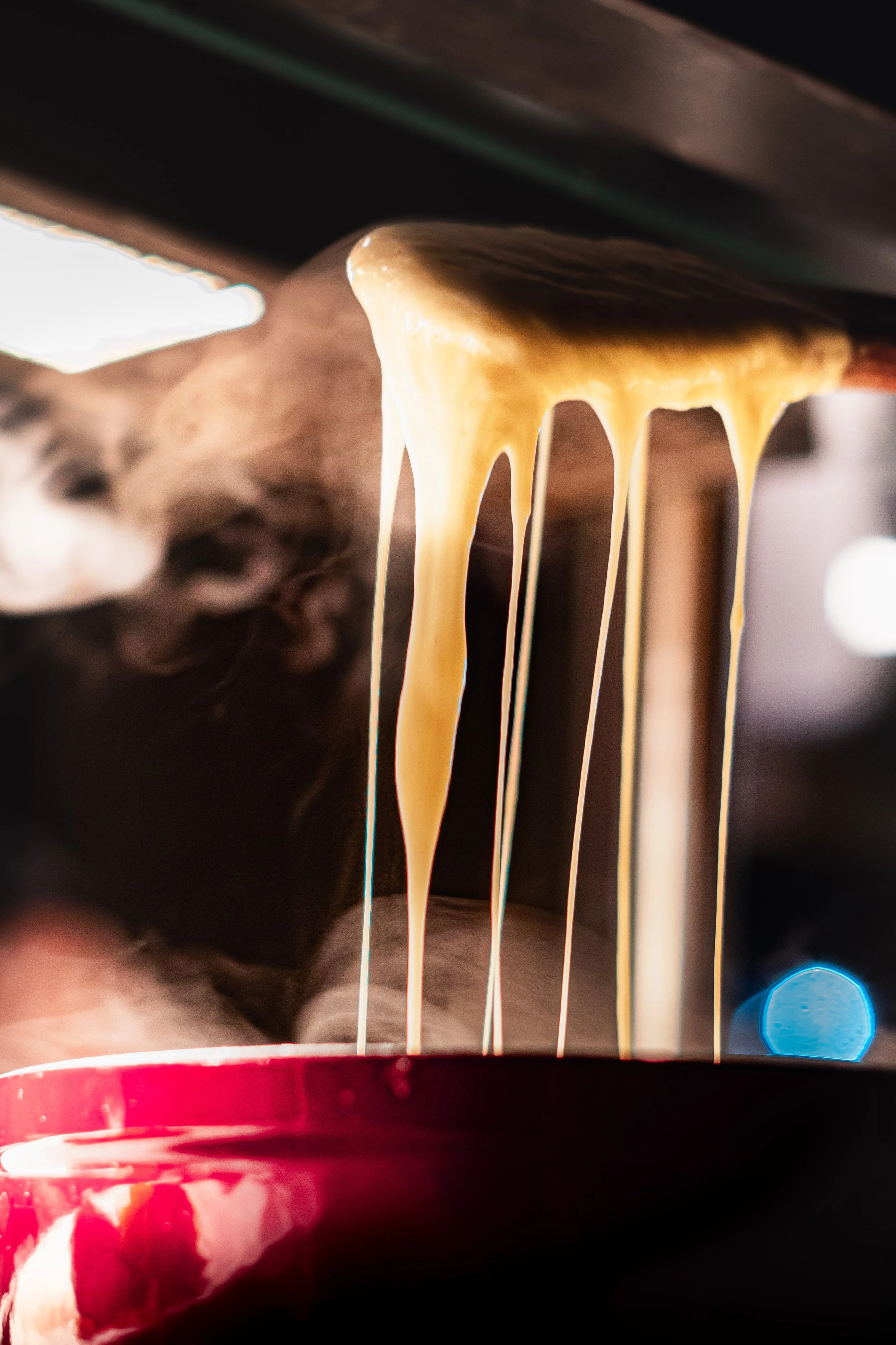 Fromage fondu qui file d'une cuillère dans un caquelon à fondue rouge.