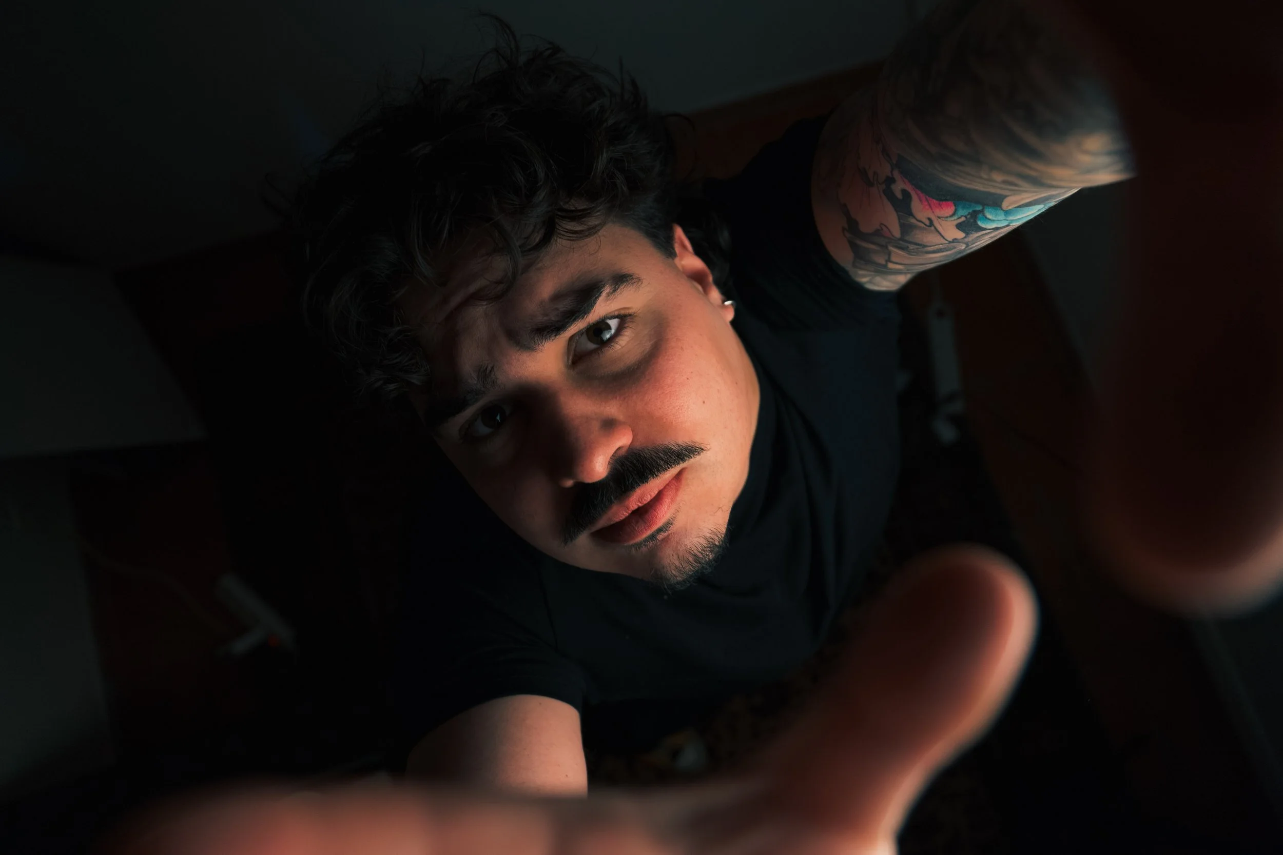 Jeune homme avec tatouage sur l'épaule, regardant vers le haut en prenant un selfie.