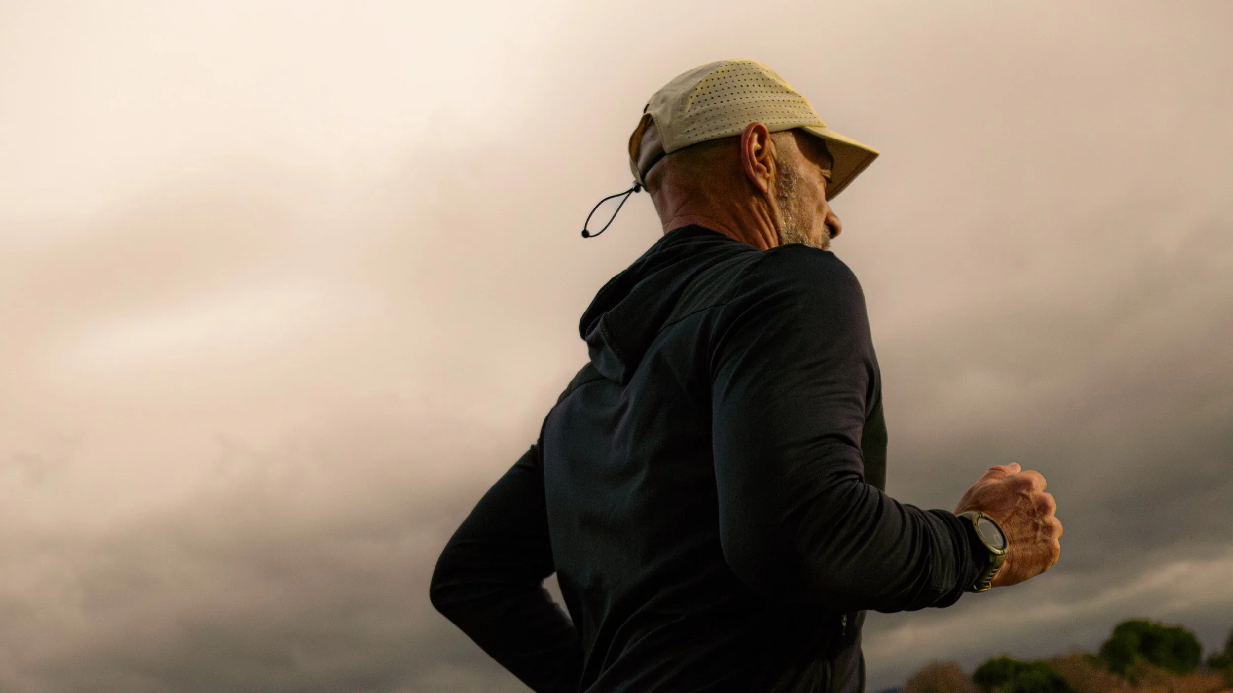 Homme courant sous un ciel nuageux, portant une casquette beige, une veste noire et une montre