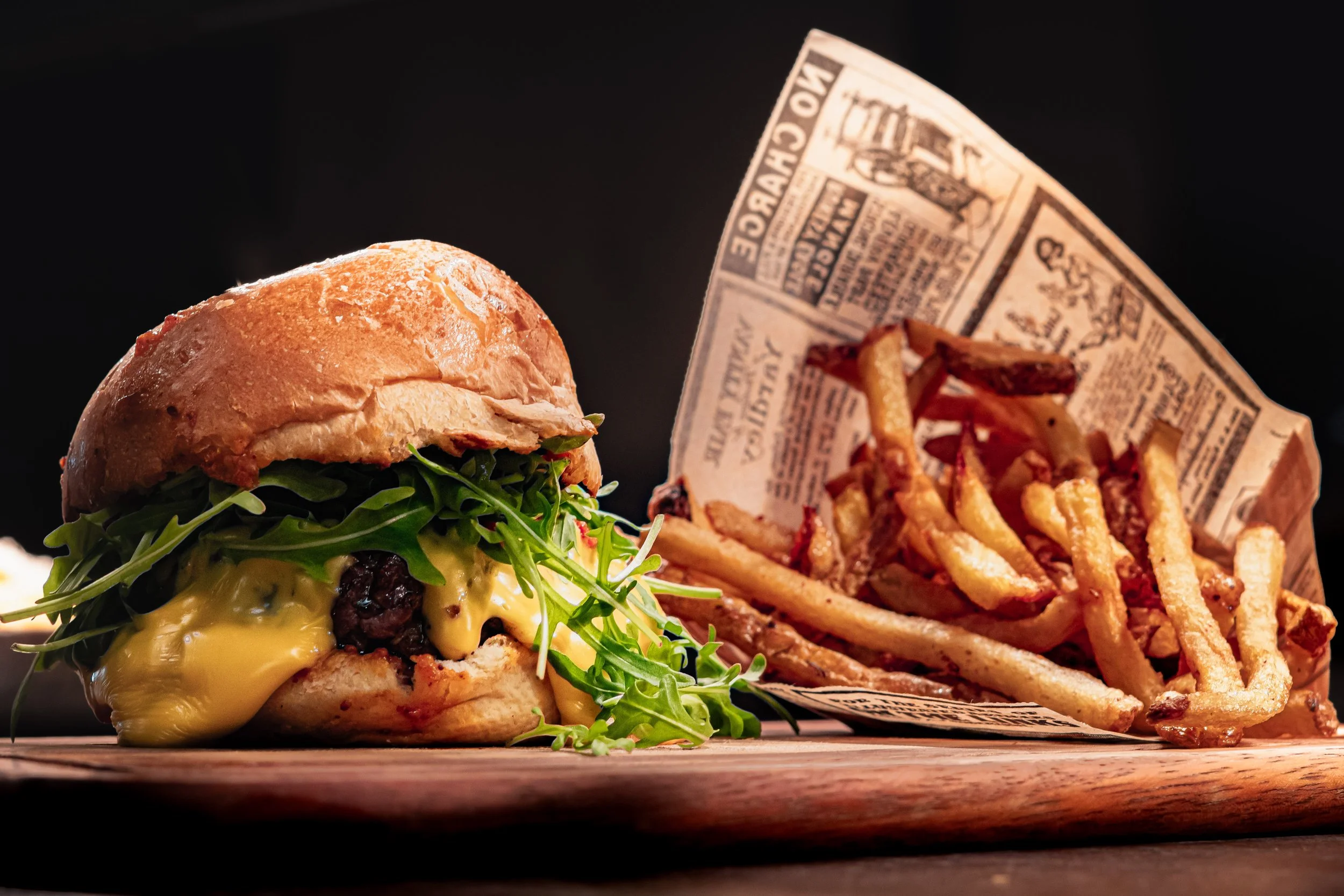 Hamburger avec fromage, salade et bacon, accompagné de frites dans un papier en papier journal.