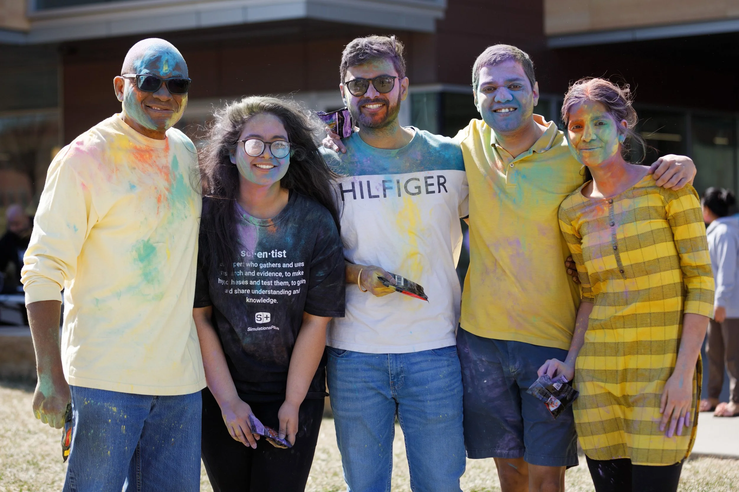 Dr. Dele Davies and students smile at camera with Holi powder on them