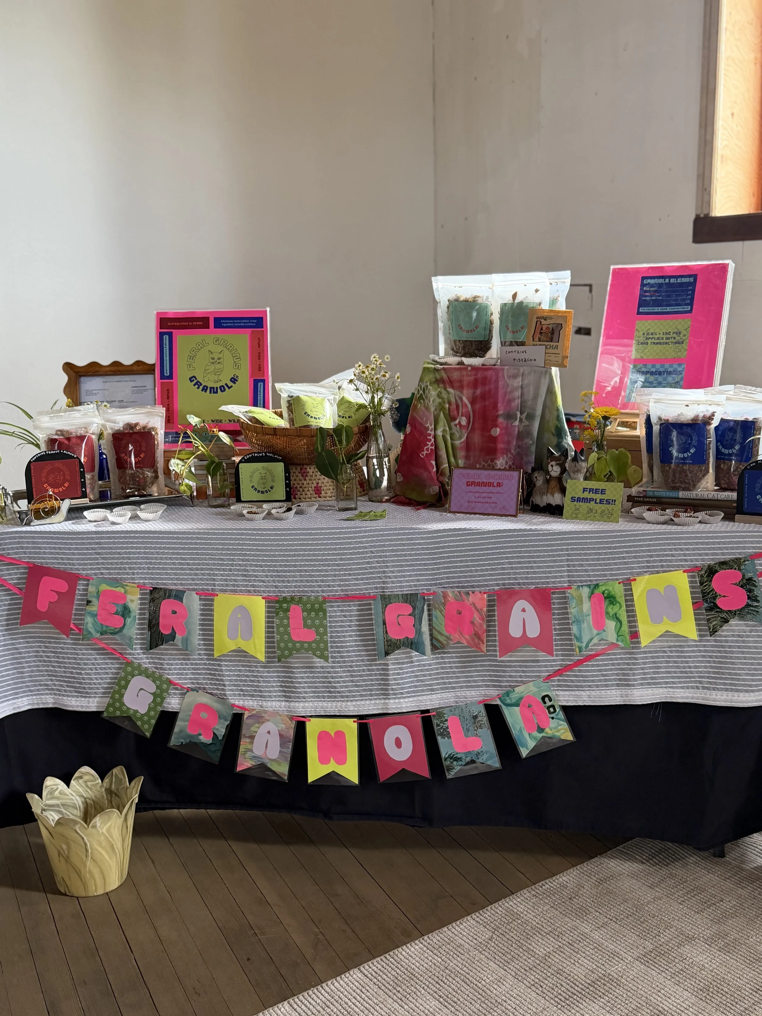 Table decorated with colorful banners reading 'Feral Friends Farewell' and various treats, signs, and small decorative items, set up for a farewell event.