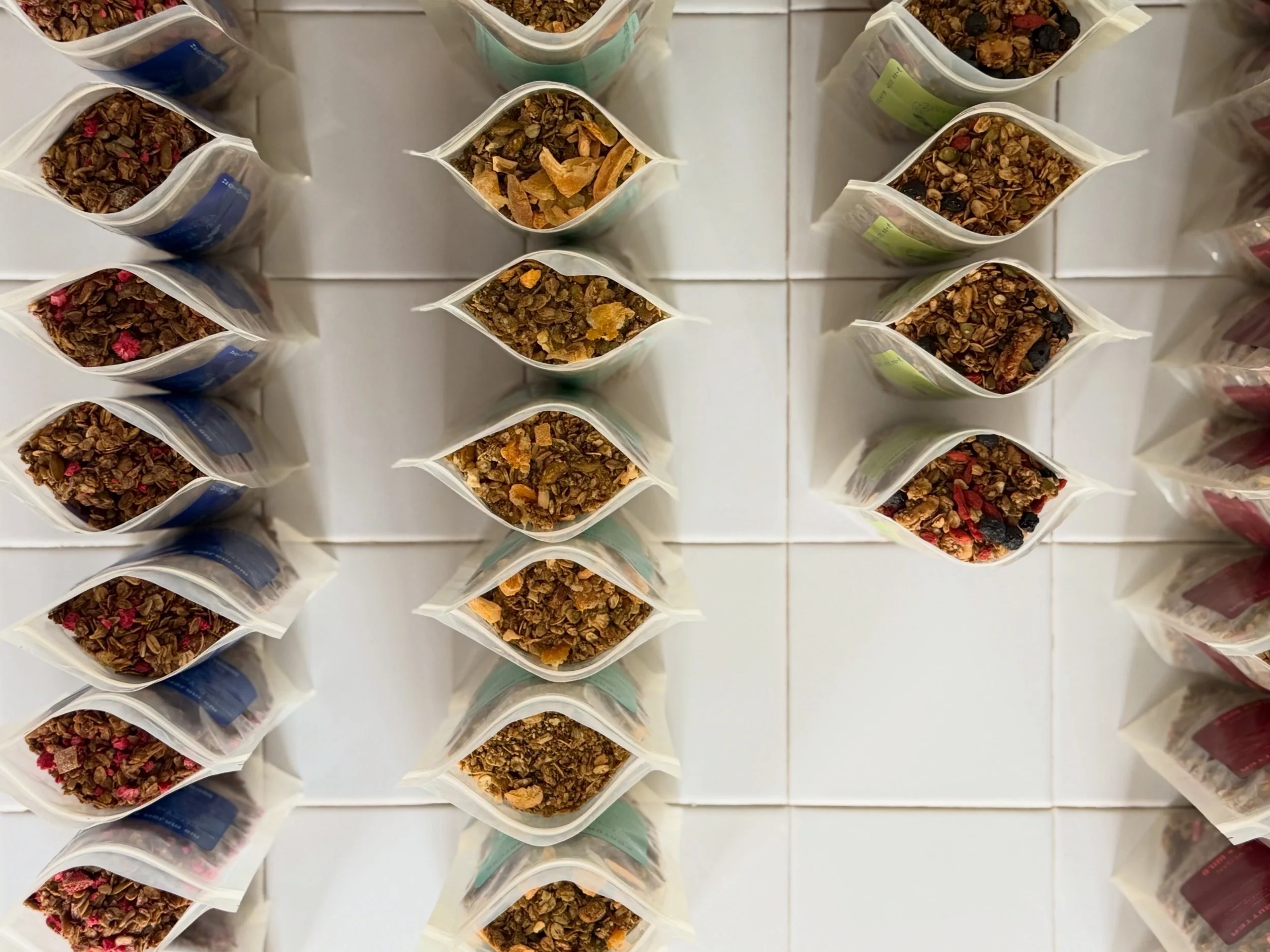 Top-down view of multiple bags of granola arranged in rows on a white surface.