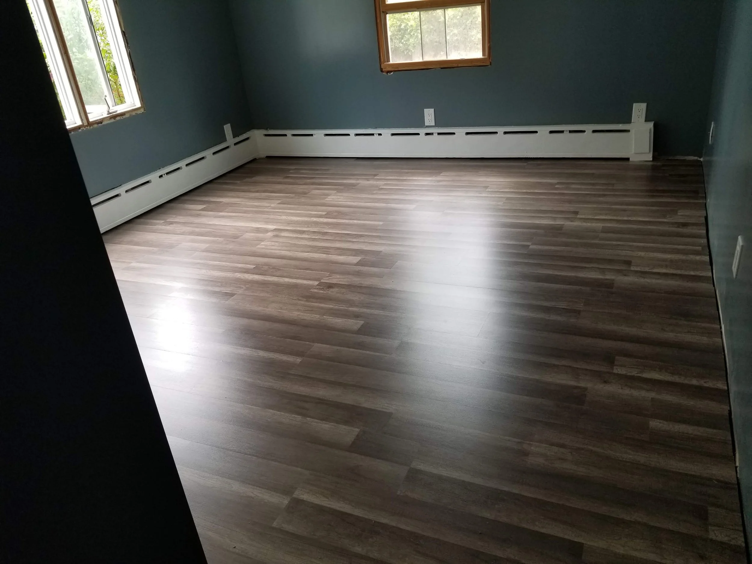 Empty room with blue walls, hardwood flooring, three windows, and a white baseboard heater.