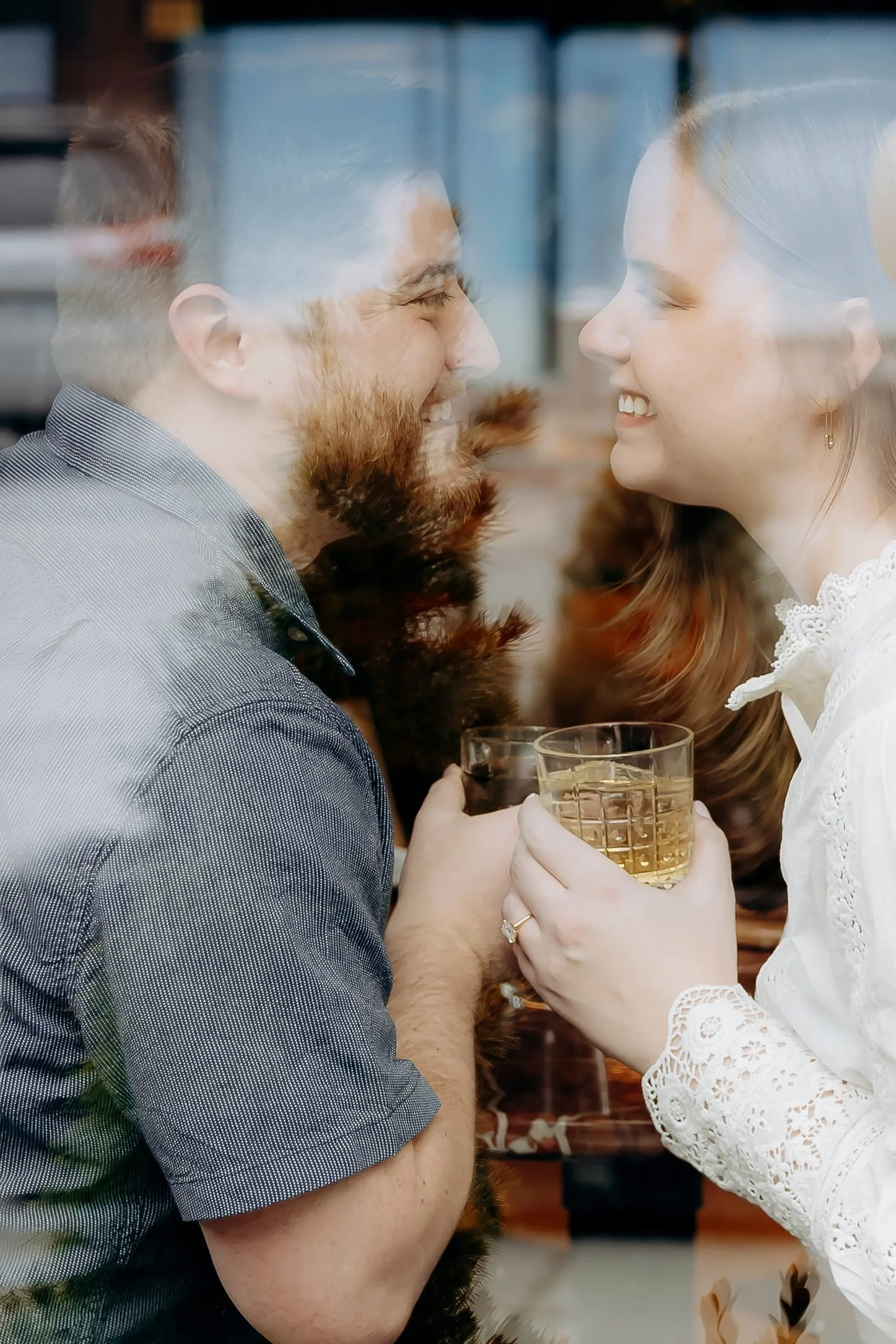 A man and a woman are smiling and looking into each other's eyes while holding a glass of whiskey. They are close together, sharing a joyful moment.