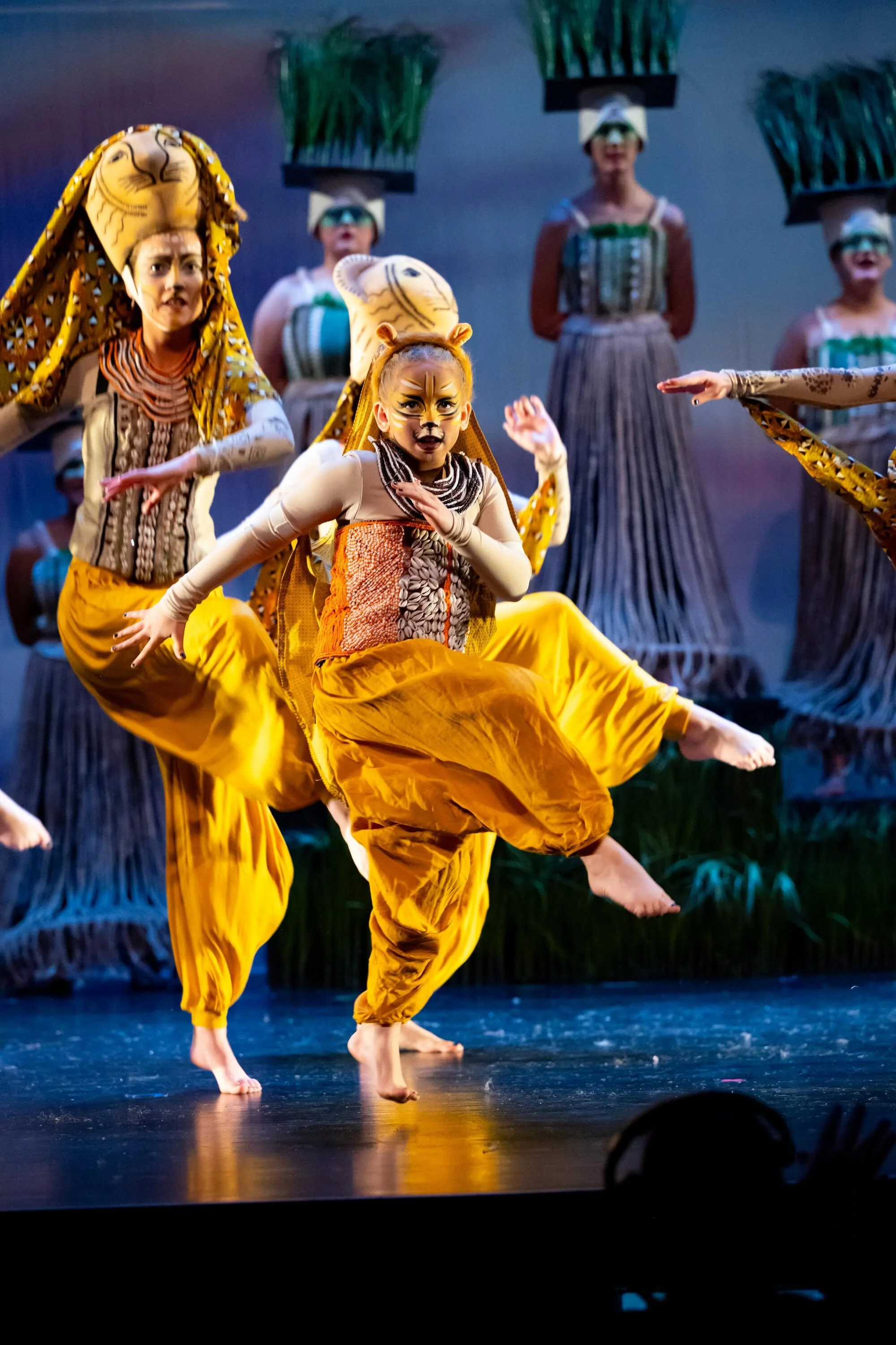 Children dressed as lions performing a dance on stage with a jungle-themed backdrop.