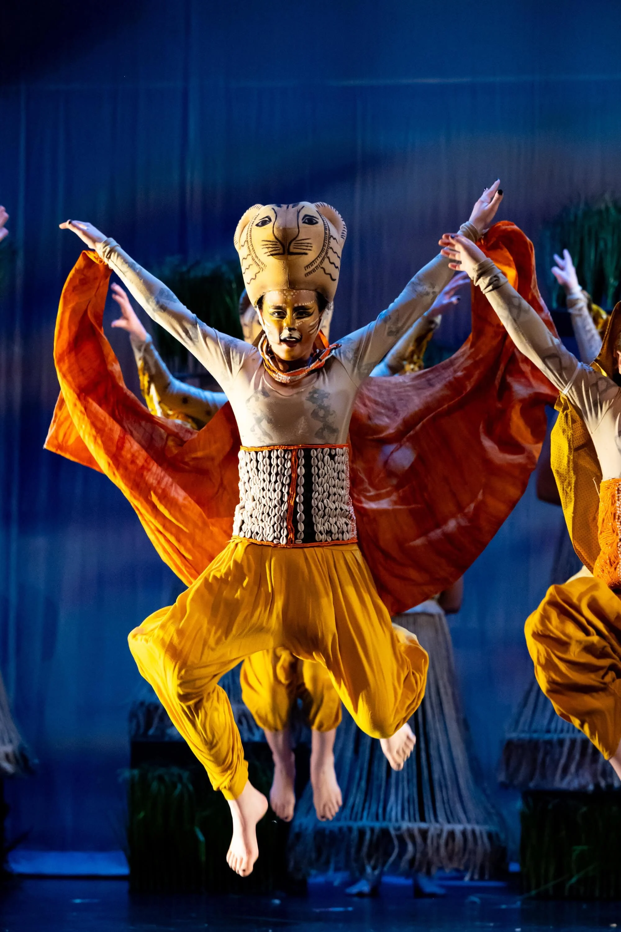 Performer in lion costume jumping with arms outstretched during a stage performance.