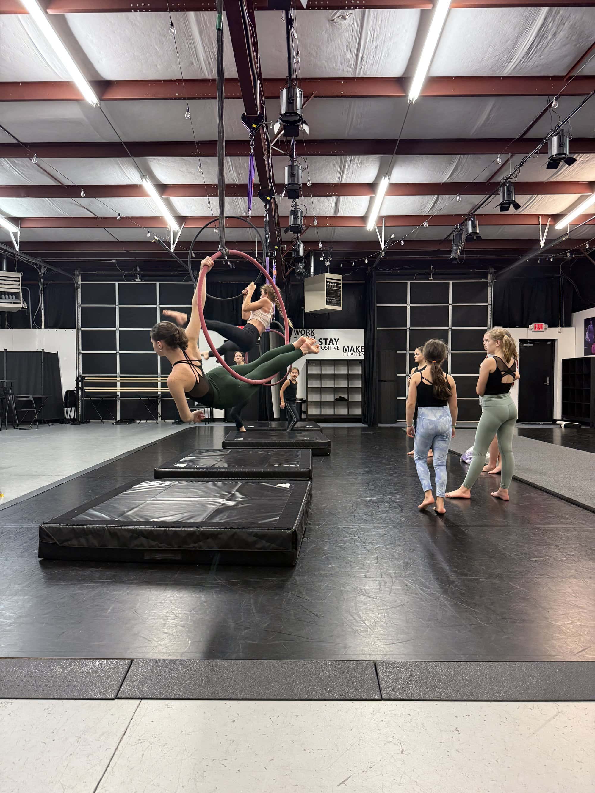 Aerial acrobats practicing on aerial hoops in a dance studio with several onlookers.
