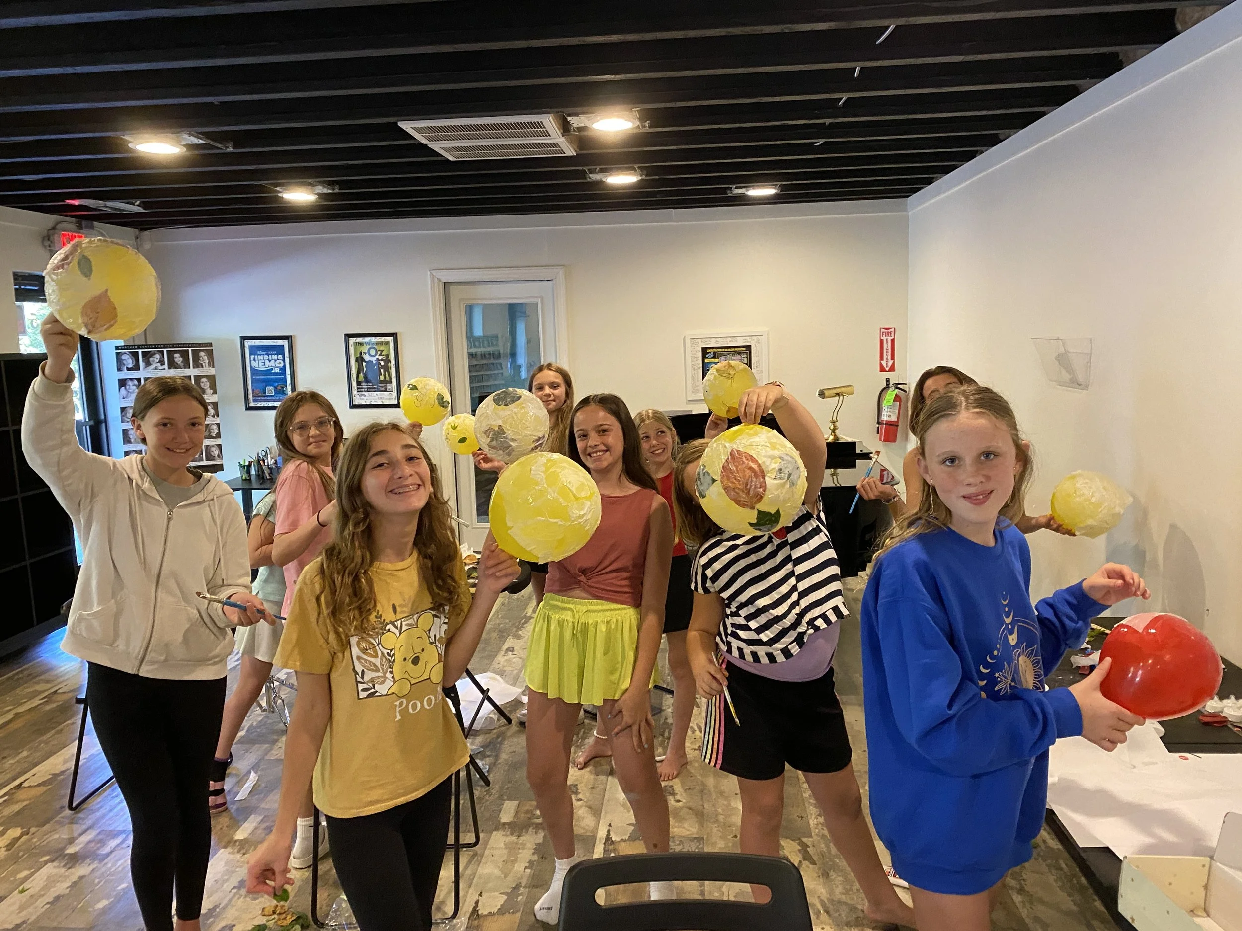 Group of young girls in an indoor art studio holding decorated paper mache globes and balloons.