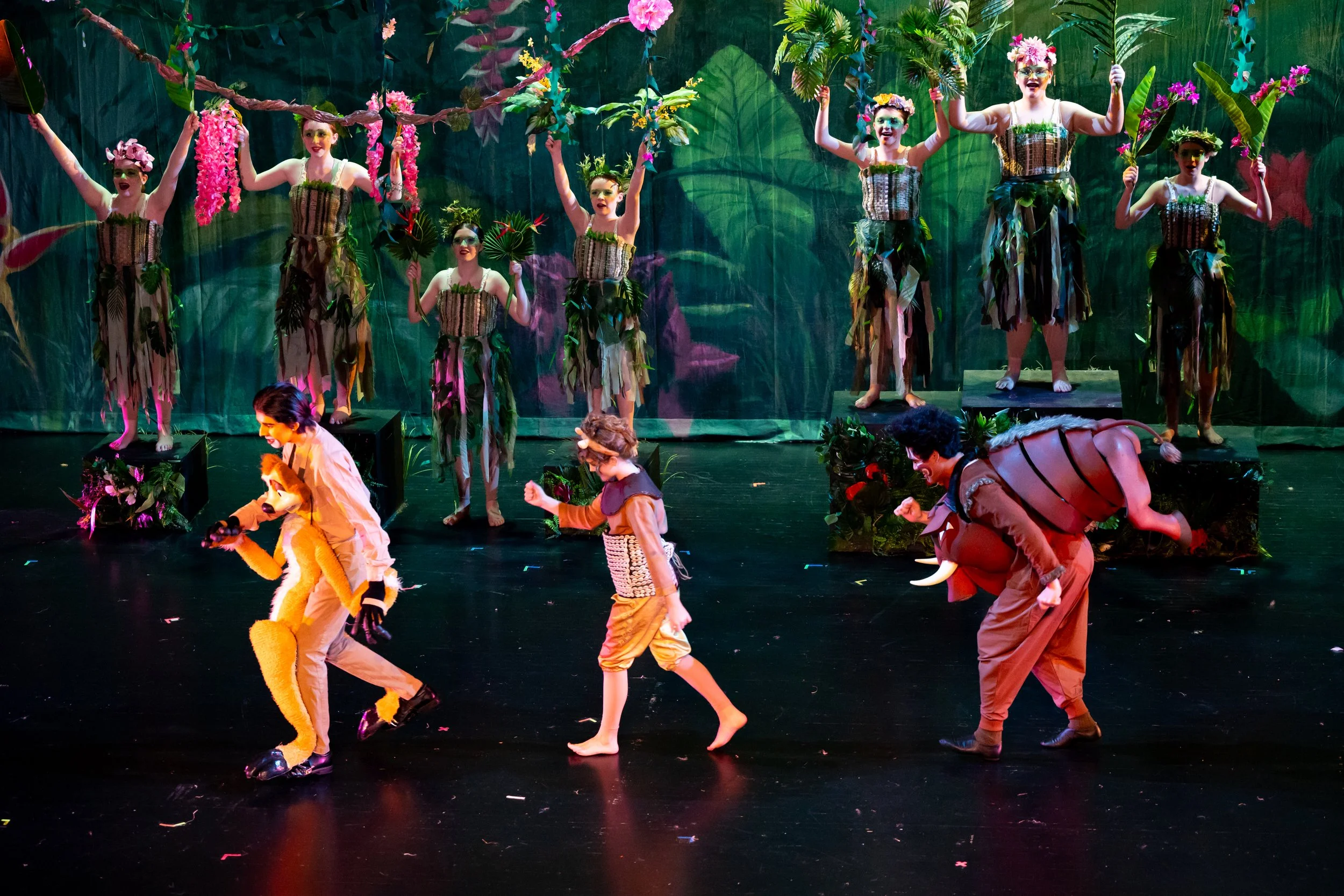 Timon, Pumbaa, and Simba sing and dance on stage in "Hakuna Matata" during "The Lion King JR" with Asheville Junior Theater, AJT. Puppetry, professional costumes and glorious sets in this professional musical theater show. The actors in the backgroun