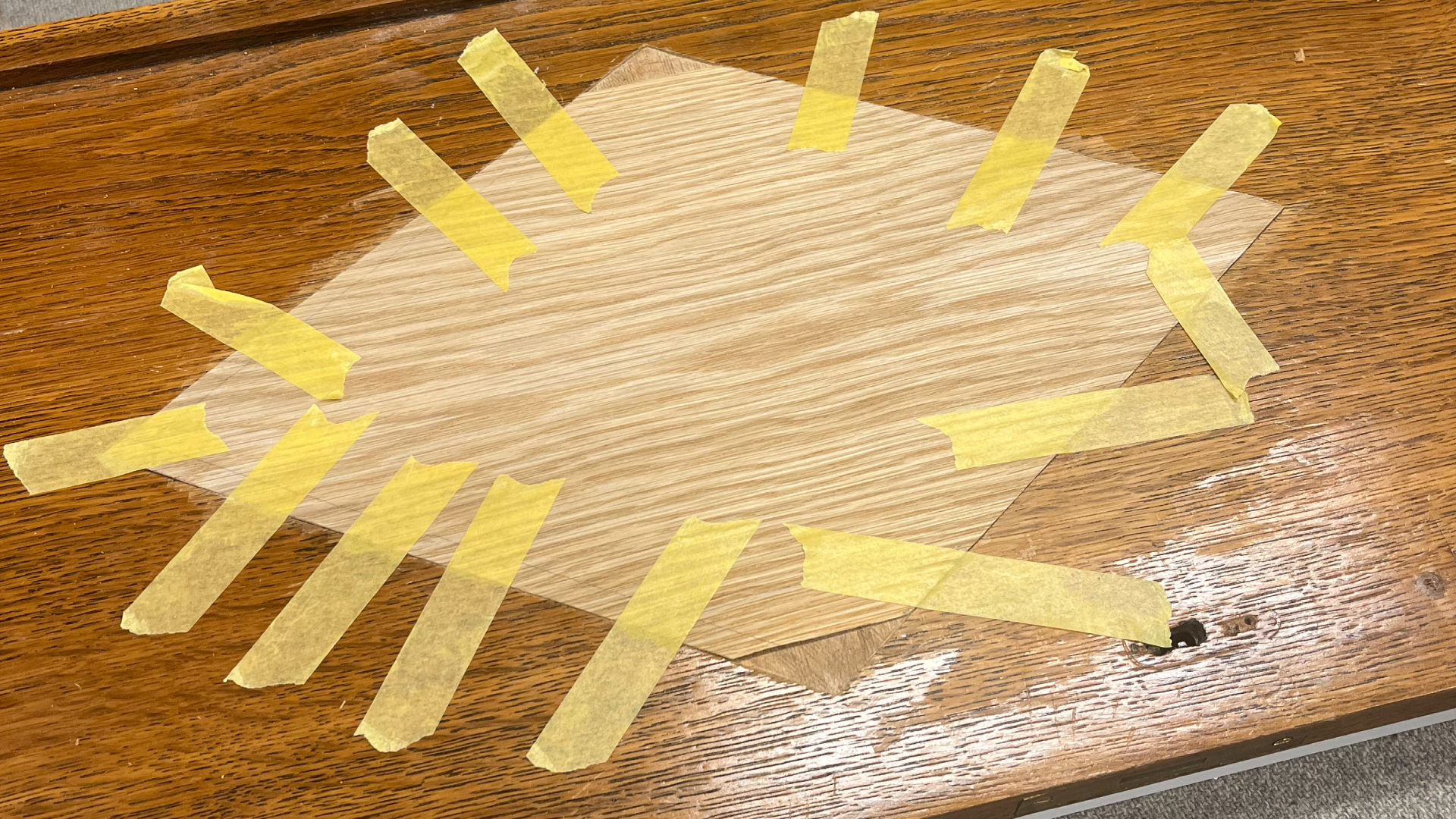 A piece of wood on a wooden table with yellow painter's tape surrounding it.