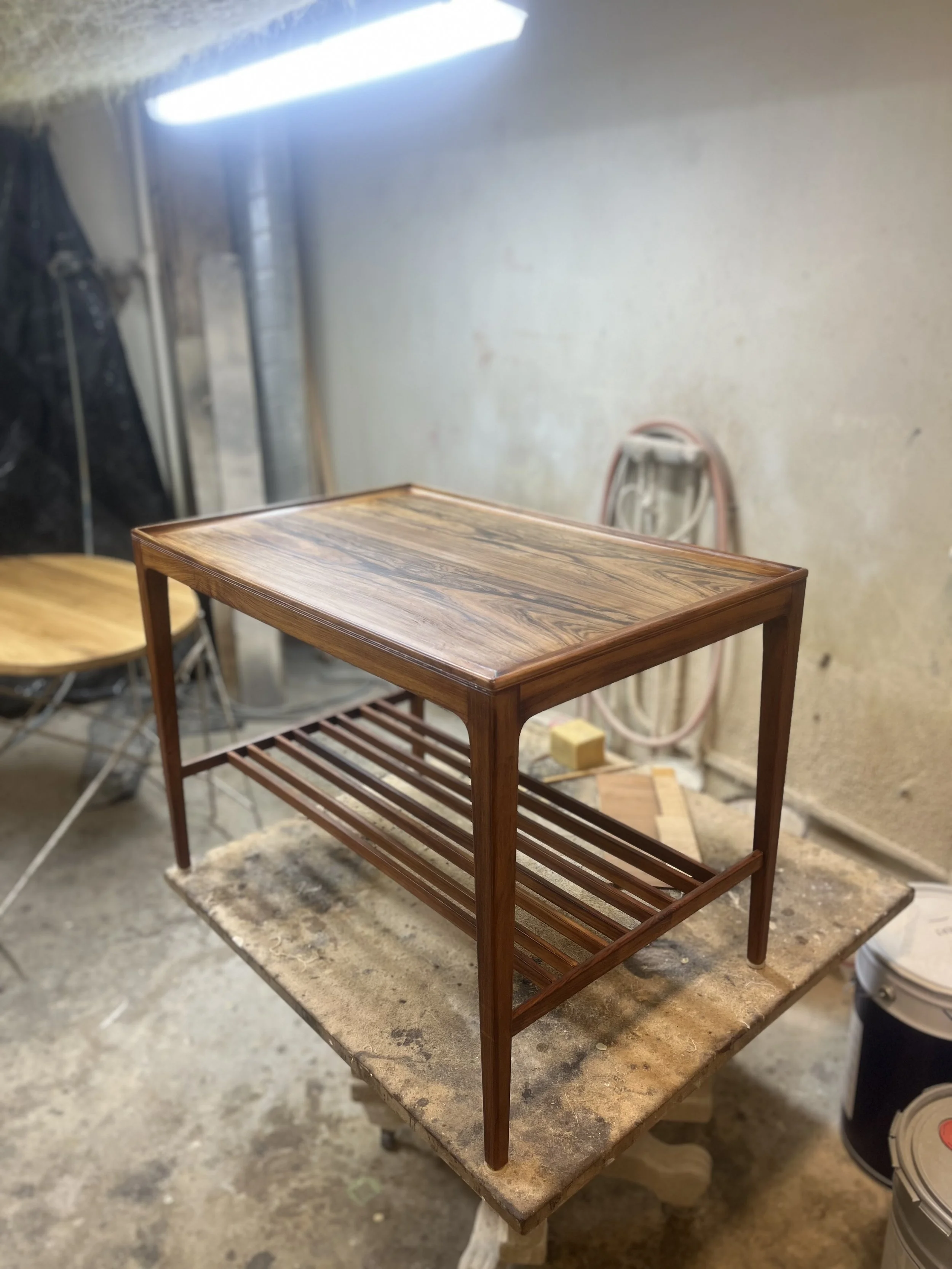 A wooden side table with a geometric pattern on the top, standing on a workbench in a workshop or carpentry shop.