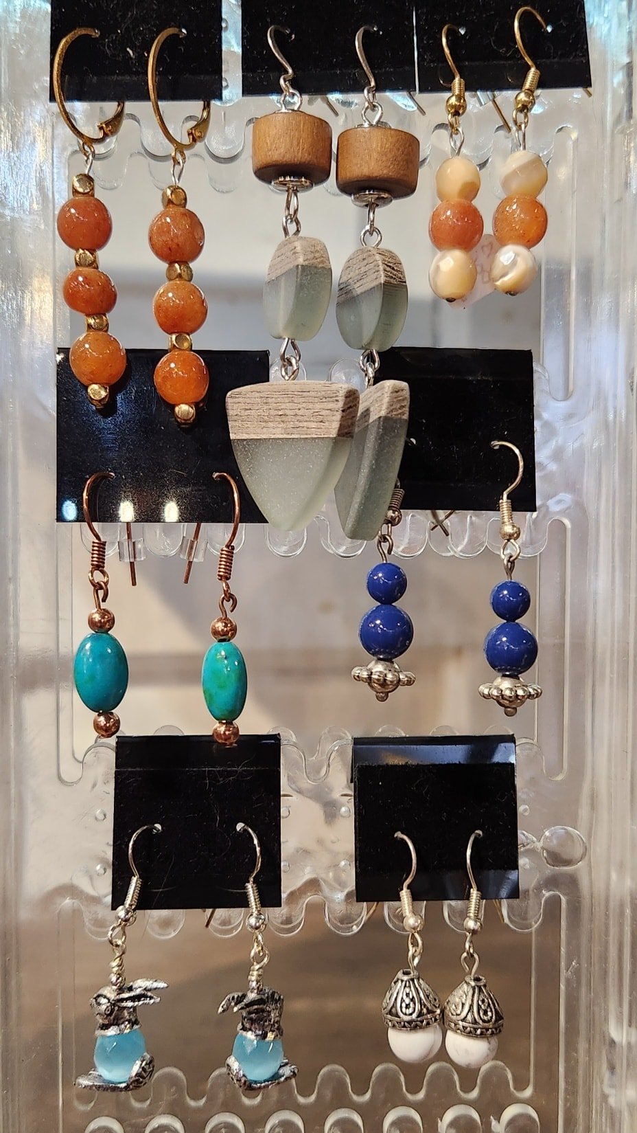 Display of various handmade earrings including orange bead earrings, wooden and stone bead earrings, blue bead earrings, and white and silver bunny and mushroom designs.