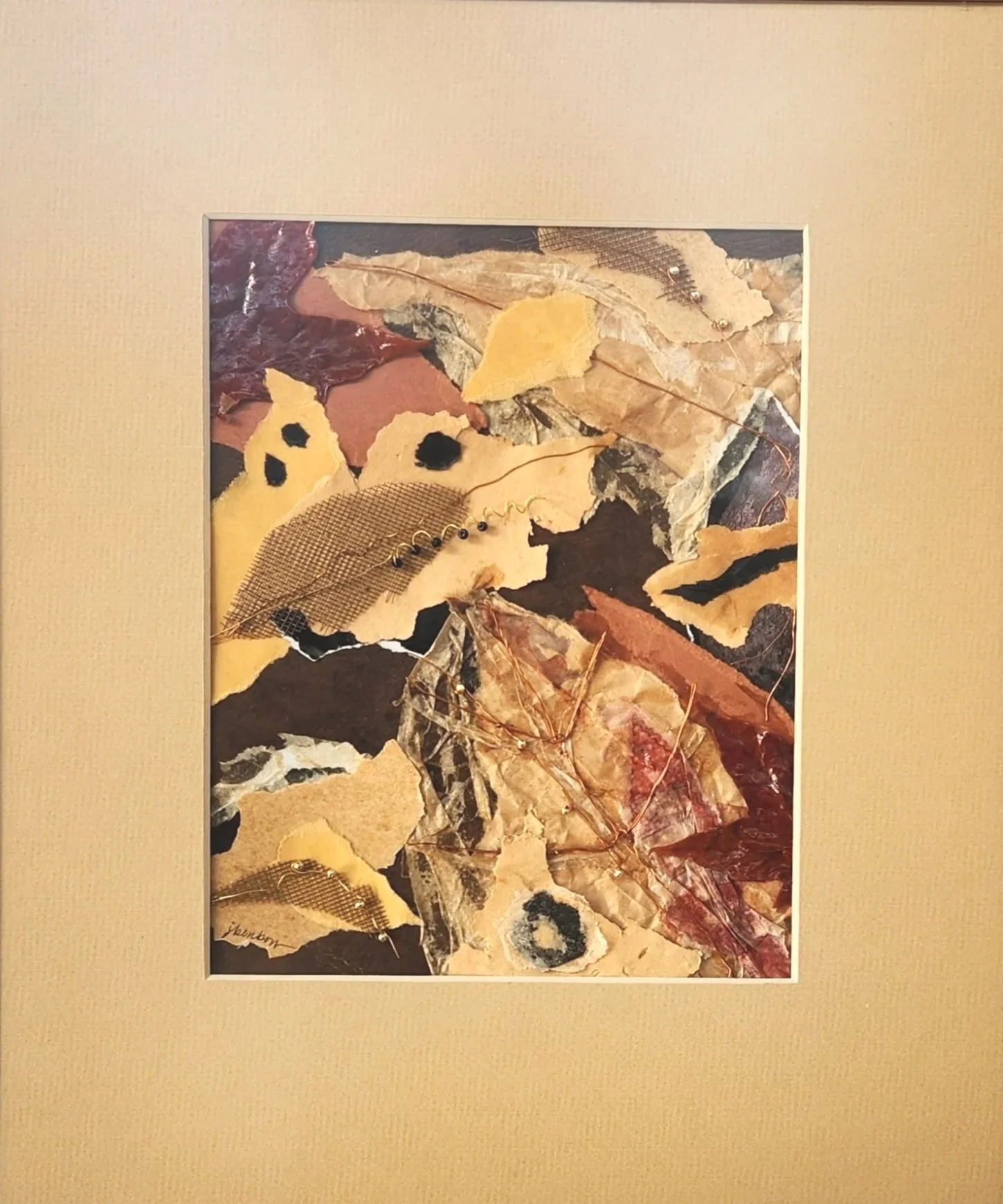 A framed collage of various dried leaves, some with black spots, some with holes, and some with stitches, arranged on a beige background.