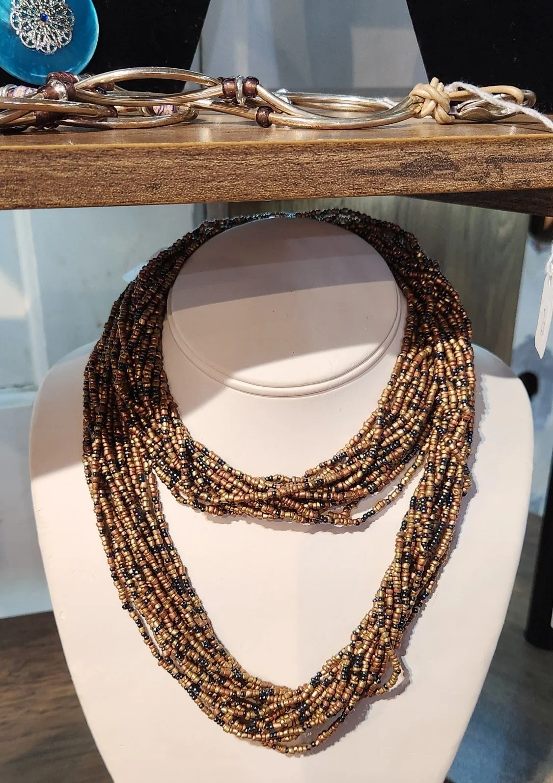 A multi-strand beaded necklace with brown, gold, and black beads displayed on a white necklace stand.