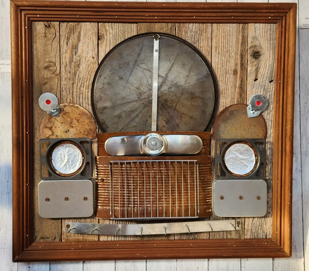 Upcycled art piece resembling a vintage car dashboard, mounted on a wooden background within a wooden frame.  Created by artists Joyce and Ken Benbow, located at the Community Art Center of Switzerland County in Vevay, Indiana