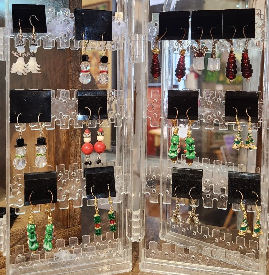 Display case with Christmas-themed earrings, including gifts, Santa, Christmas trees, and snowmen.