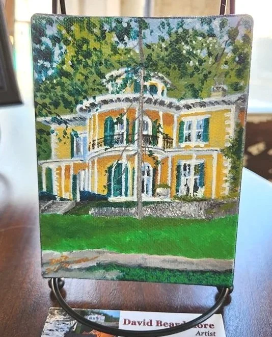 Painted miniature landscape of a yellow and white building with blue shutters, surrounded by green trees and grass.