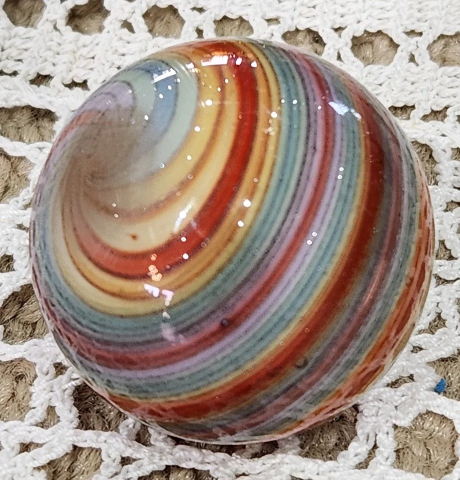 A multicolored marbled glass marble on a white crocheted surface.