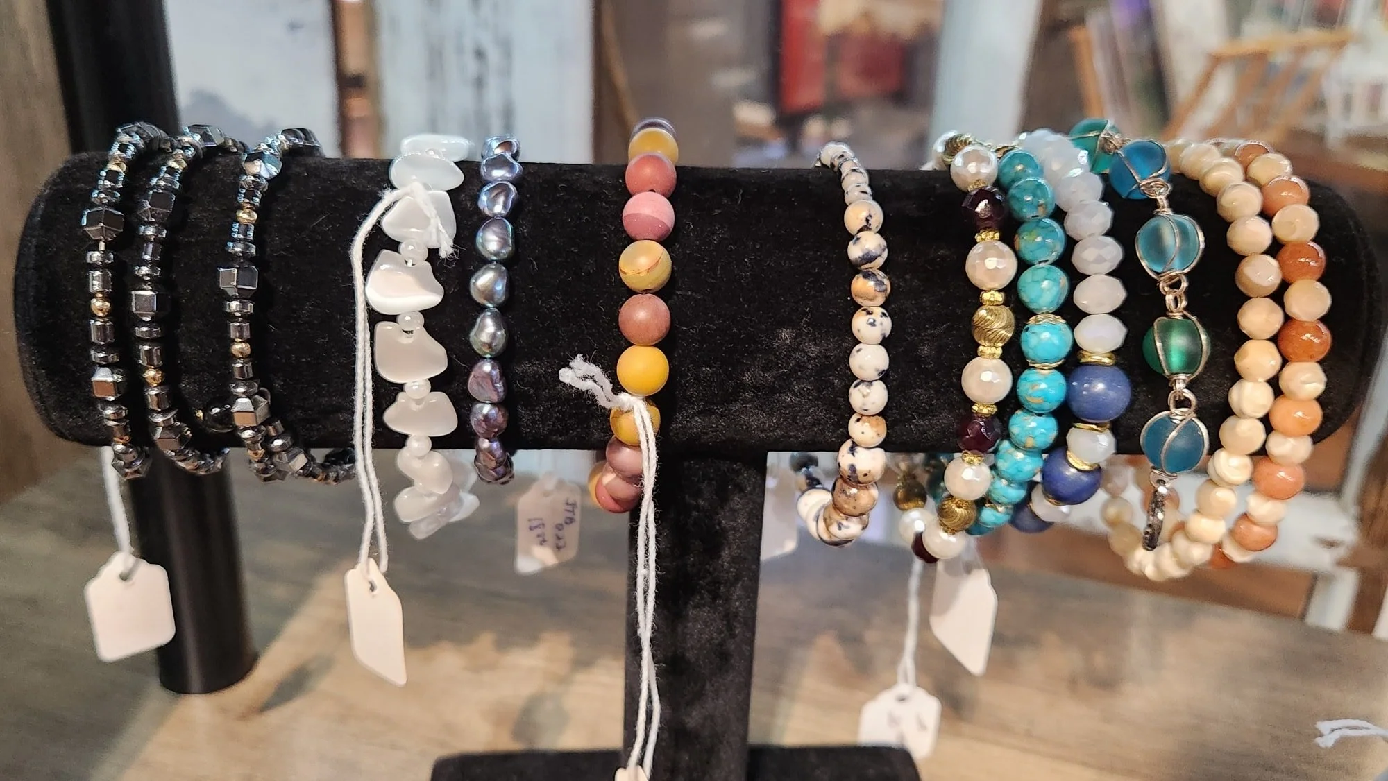 Assorted beaded bracelets displayed on a black stand, featuring various colors including black, white, purple, yellow, turquoise, blue, green, and orange.
