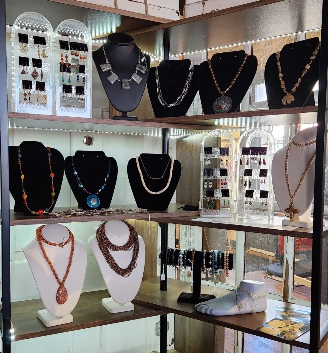 Display of various jewelry including necklaces, earrings, bracelets, and rings arranged on black and white busts and stands in a showcase at a jewelry store.