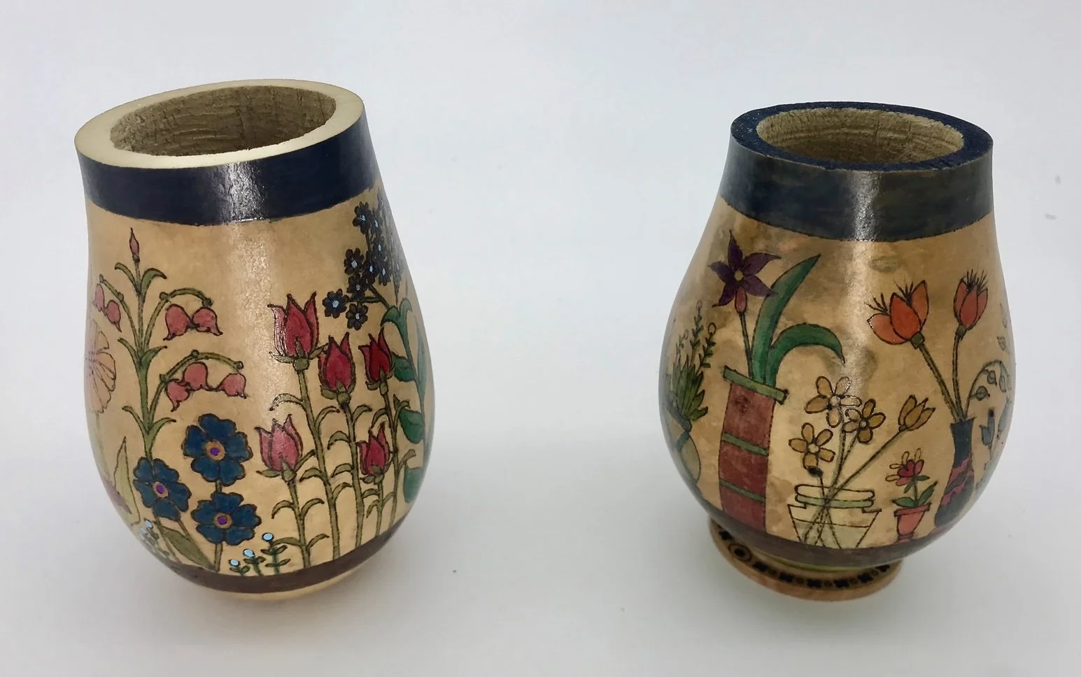 Two small decorative vases with floral painted designs on light backgrounds, black rims, and round bases.