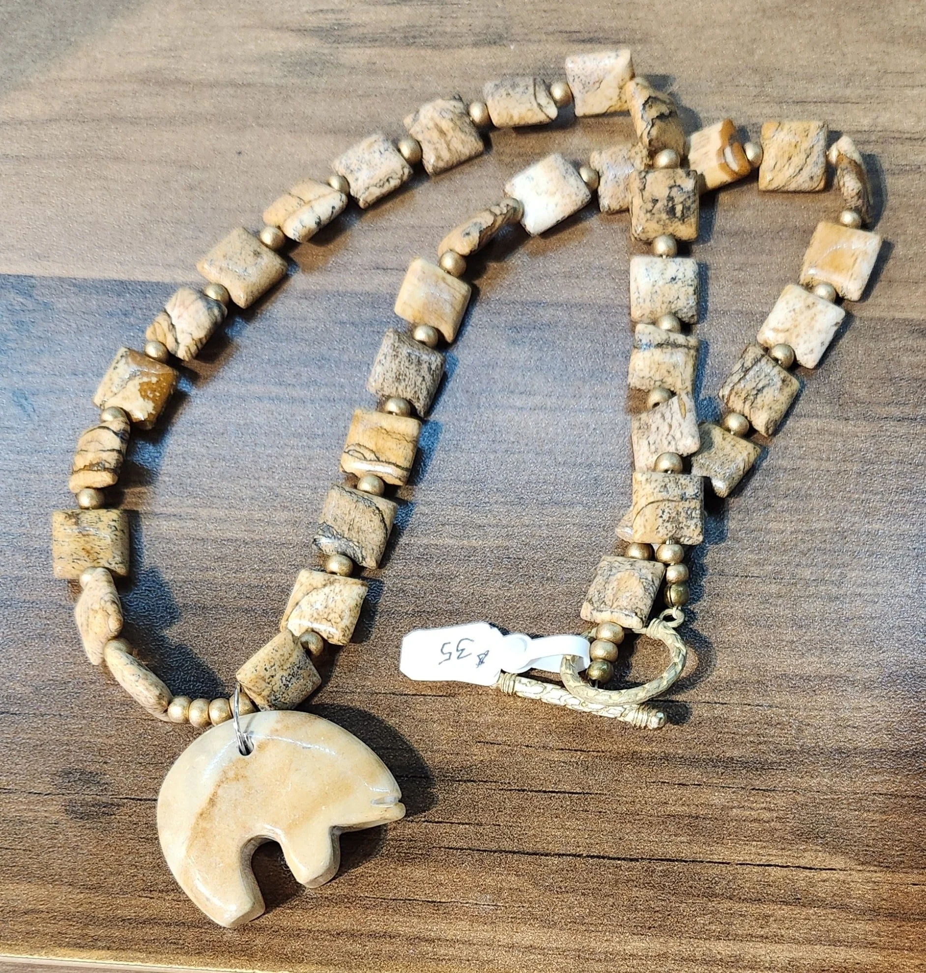 Beaded necklace with square and round stone beads and a large beige elephant pendant, lying on a wooden surface.