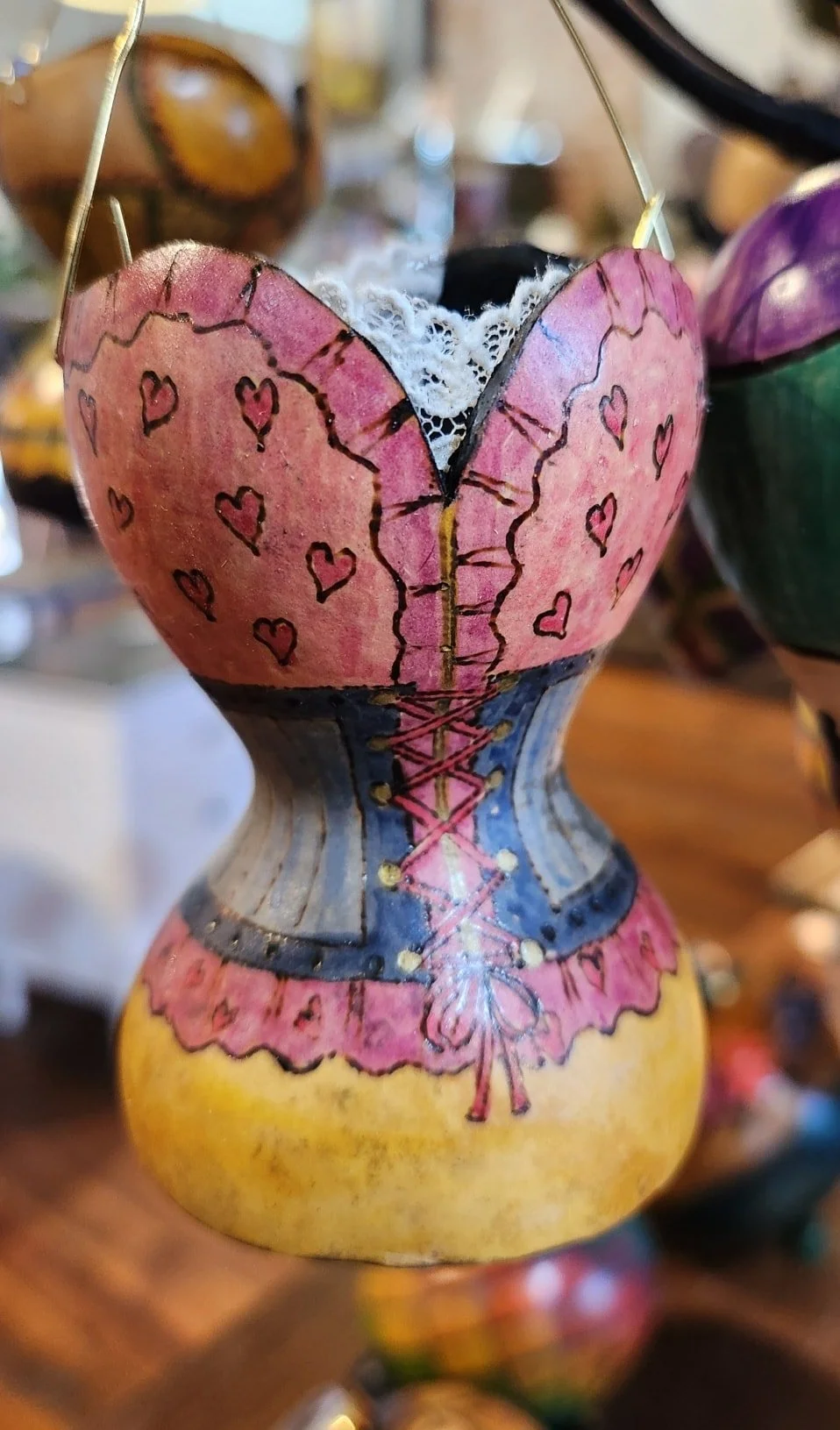 Decorative doll shaped like a ballet dancer with a heart-shaped torso painted pink, decorated with small hearts and lines, wearing a blue and grey tutu, and yellow base.