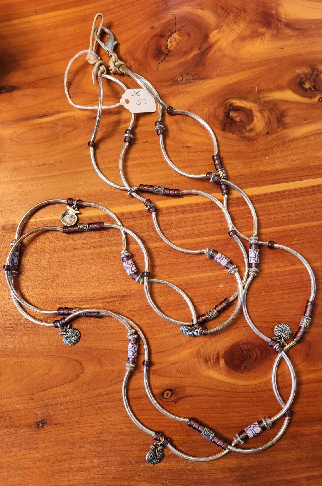 Three silver necklaces with decorative beads and charms laid out on a wooden surface.