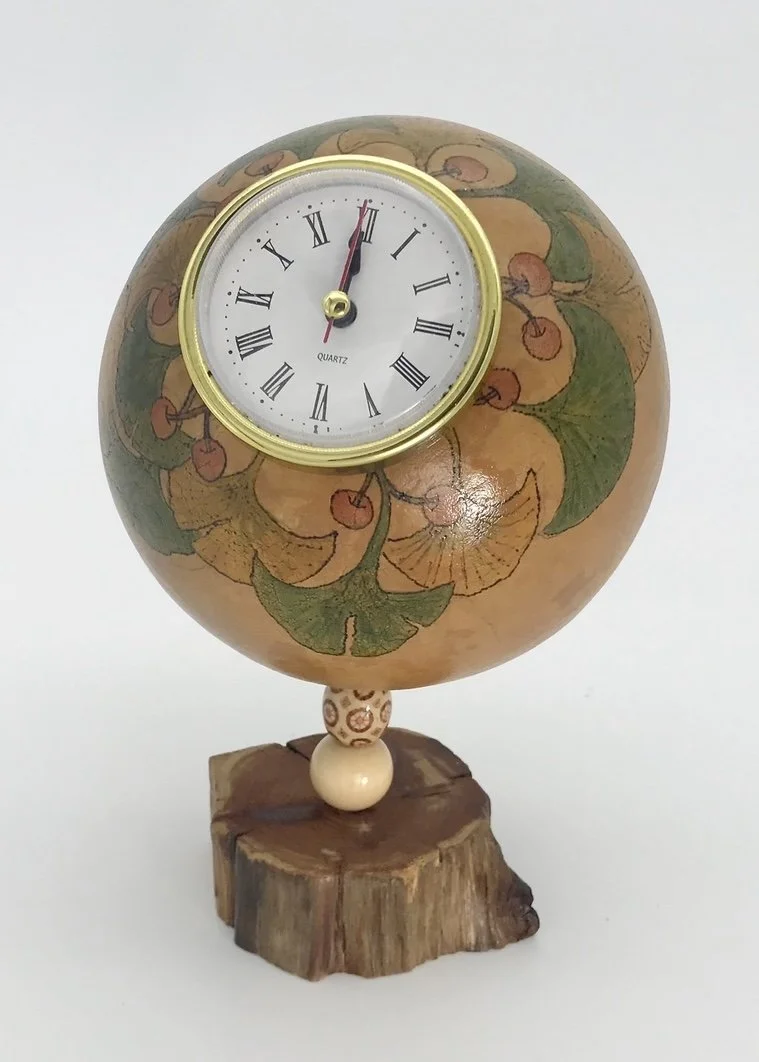 Decorative clock with floral design on spherical surface, mounted on a wooden base.