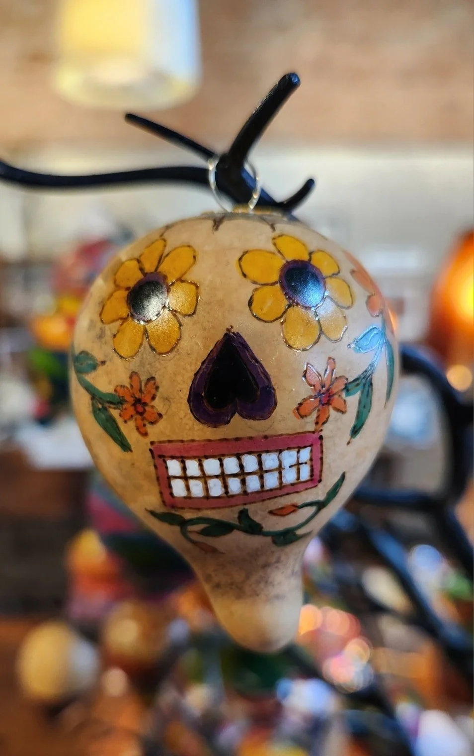 Decorative ornament designed as a colorful skull with yellow flowers for eyes, orange flowers on cheeks, a purple nose, and a pink mouth, hanging from a hook.