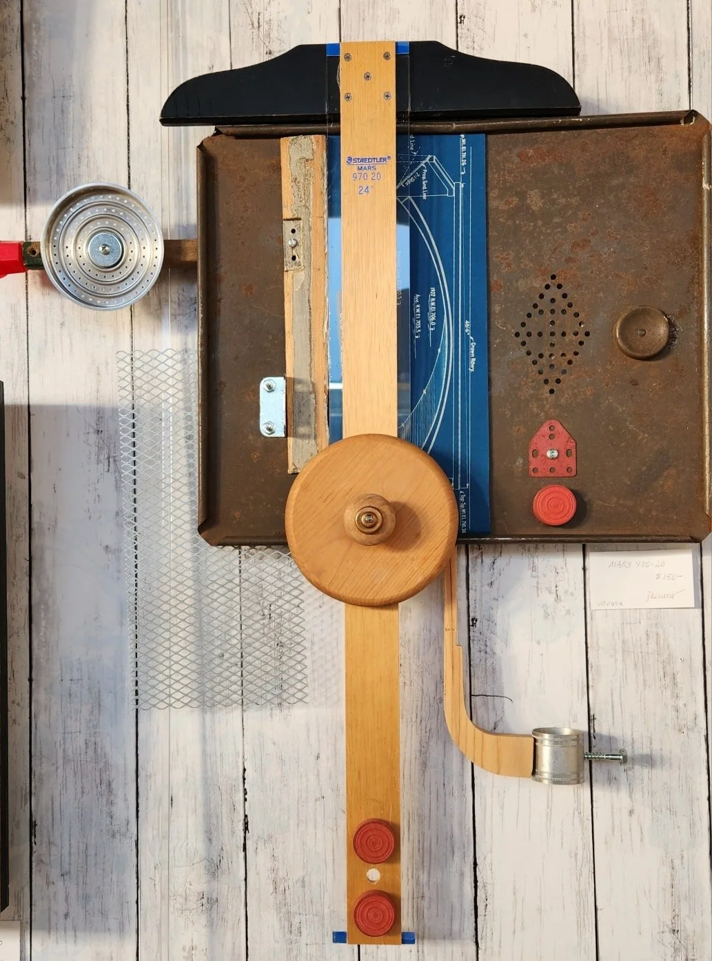 A vintage mechanical toy with a rusted metal base, a wooden wheel, and a winding mechanism on a white wooden surface.