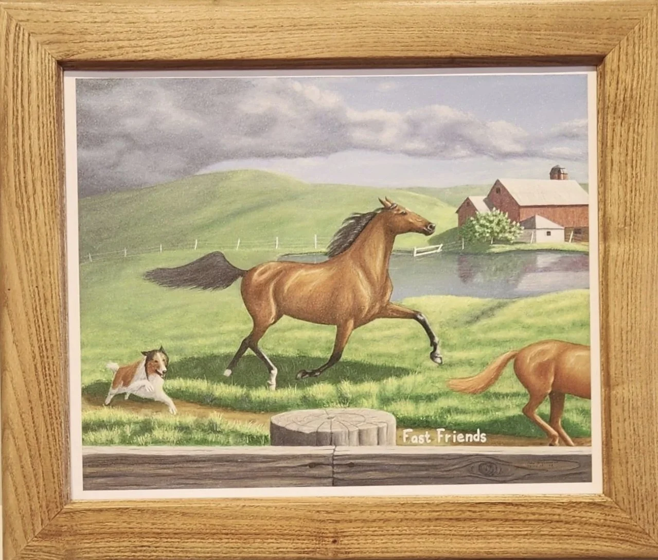 Painting of a brown horse running with a small dog chasing after it in a farm setting with green hills, a pond, and red barns in the background, framed in wood. The text "Fast Friends" is at the bottom right corner.
