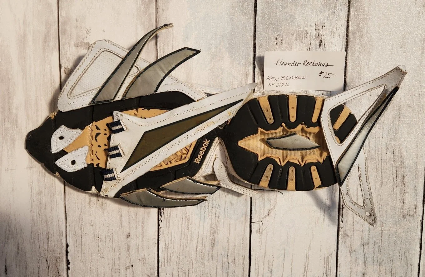Wall art of a fish sculpture made from hockey skate blades, mounted on a wooden background with a small handwritten price tag.