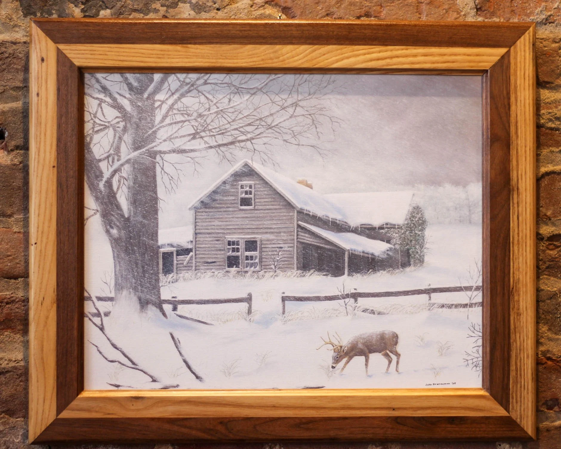 A painting of a snowy winter scene with a large tree, a rustic wooden house, and a buck grazing in the snow, framed in wood.
