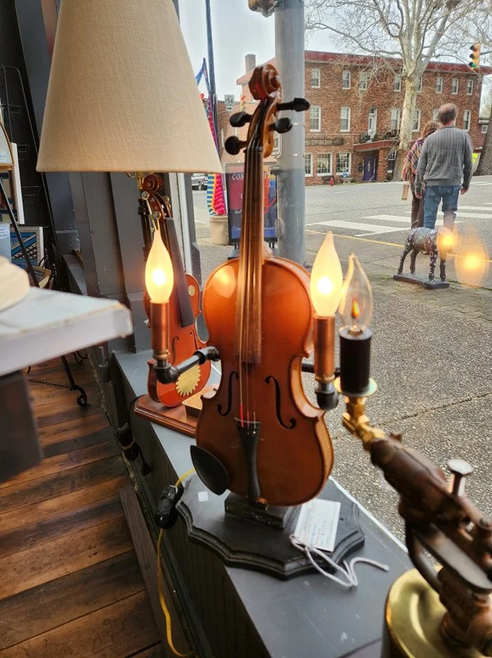 A decorative lamp shaped like a violin with candle-style light bulbs on either side, situated on a windowsill inside a shop.
